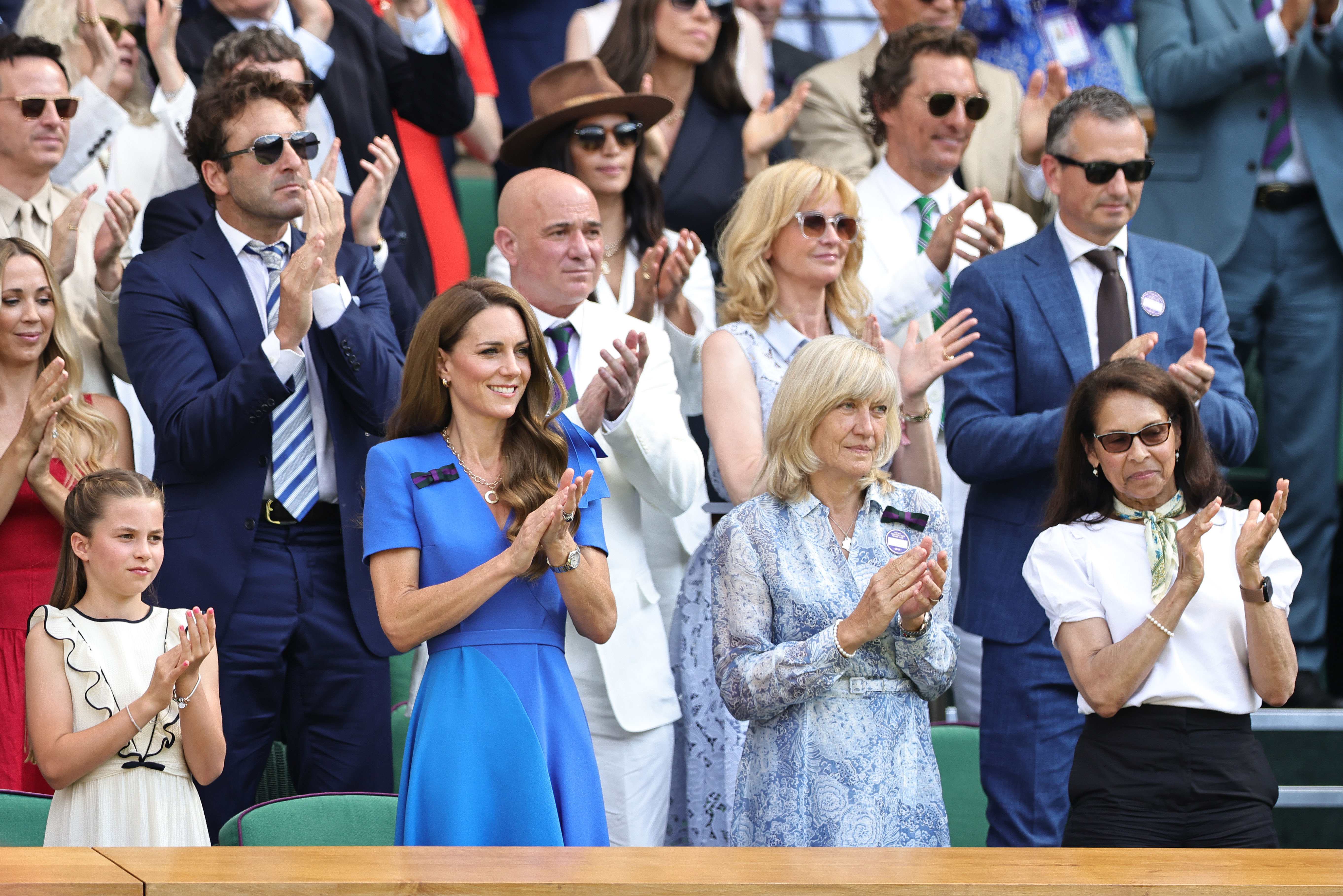 Princess Catherine stands to applaud alongside Princess Charlotte and other attendees in the Royal Box. The crowd rises behind them in celebration during a key moment of the Gentlemen’s Singles Final.