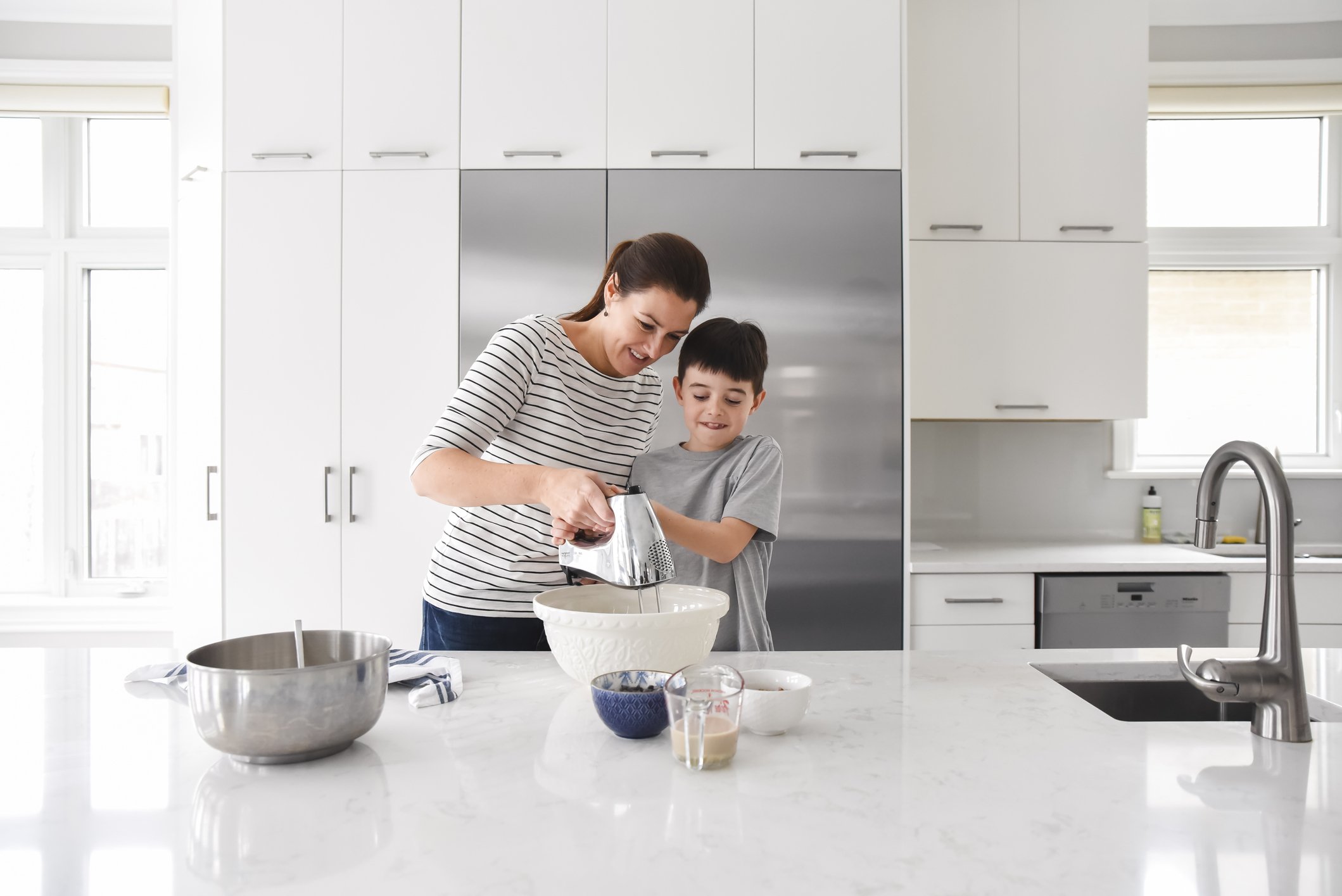 Mutter hilft dem kleinen Sohn beim Kochen in einer modernen Küche, einen Mixer zu benutzen | Quelle: Getty Images
