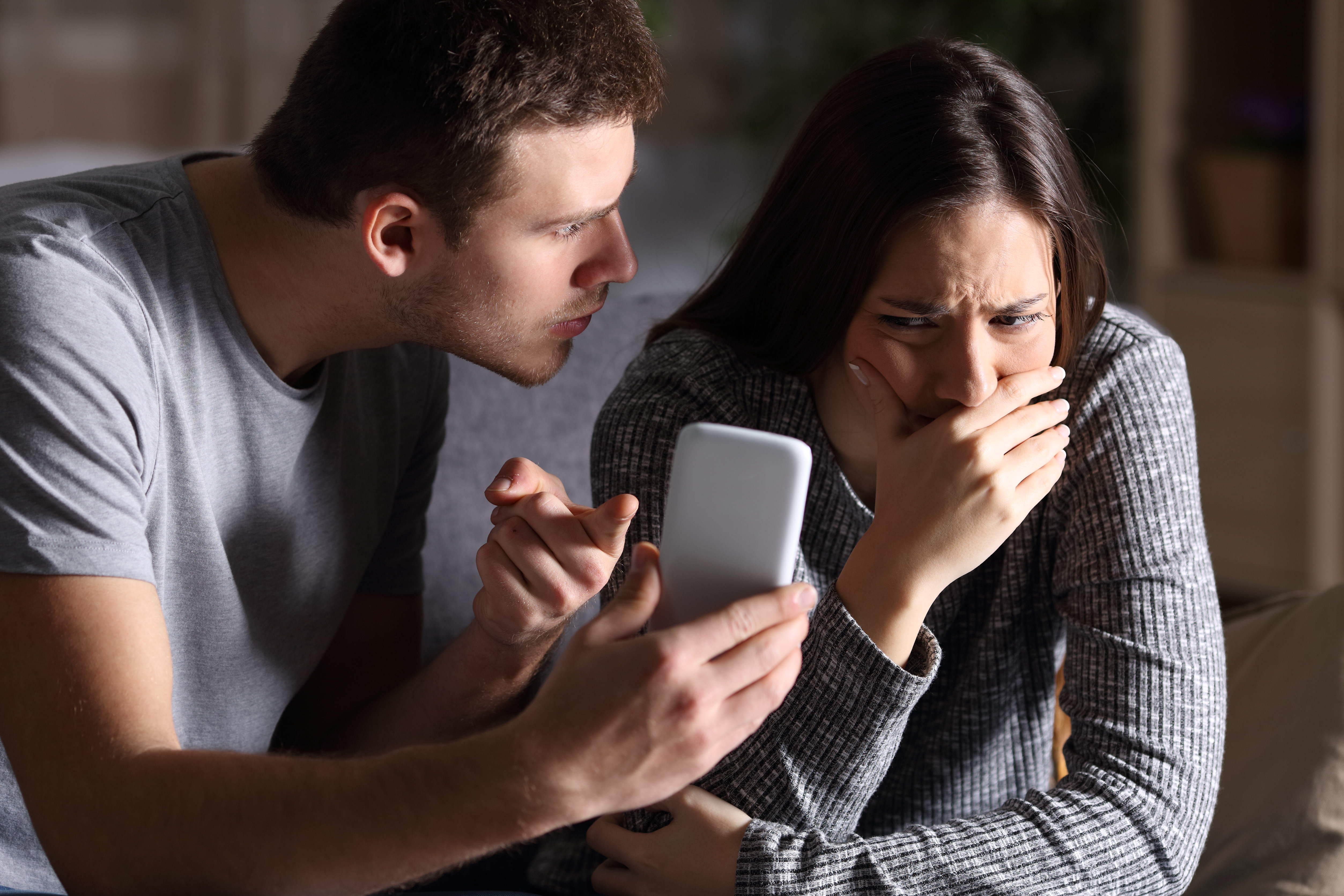 A husband asks for an explanation from his sad, cheating wife while sitting on the couch in their home. | Source: Shutterstock