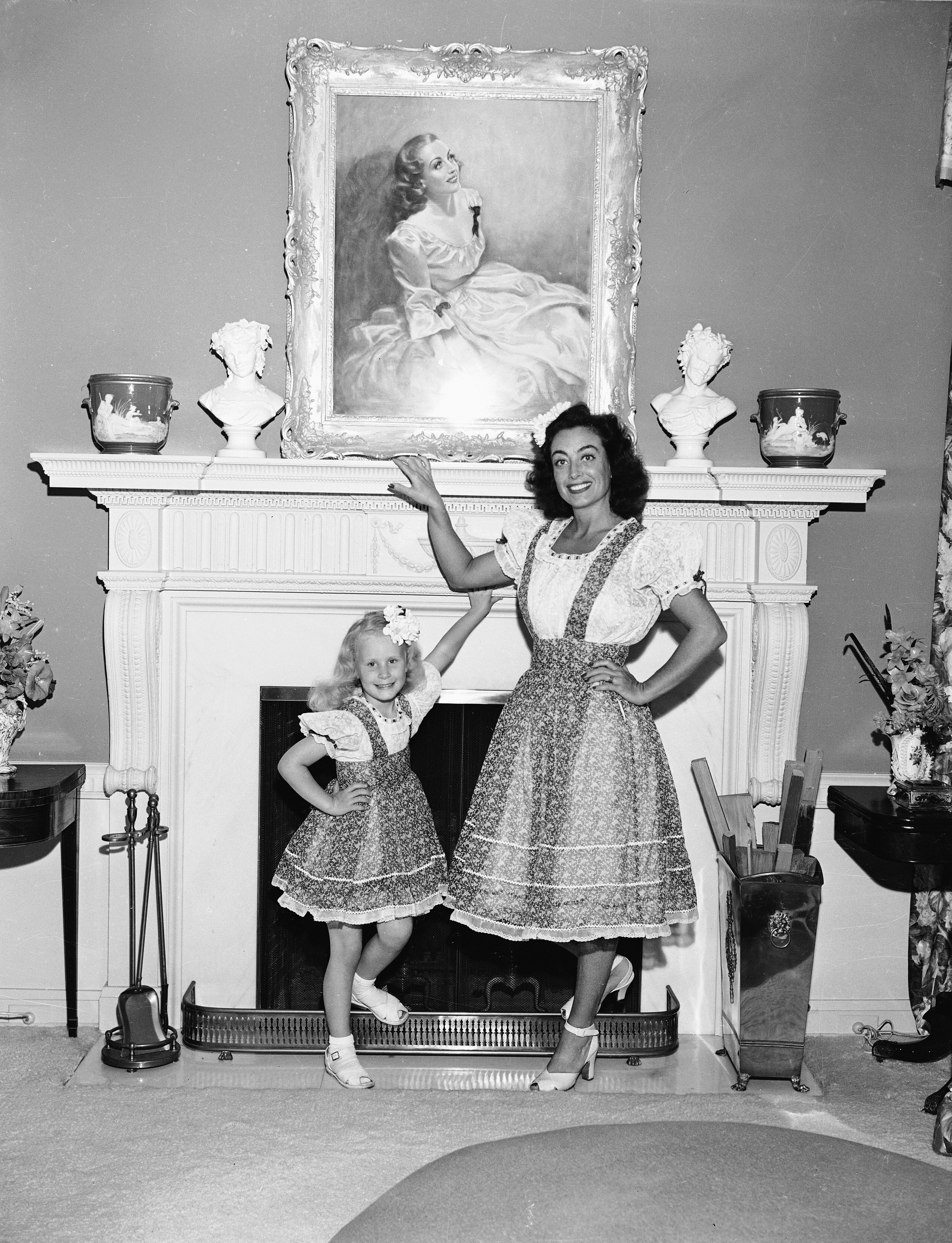Joan Crawford posing with her adopted daughter Christina next to a fireplace in June 1944. / Source: Getty Images