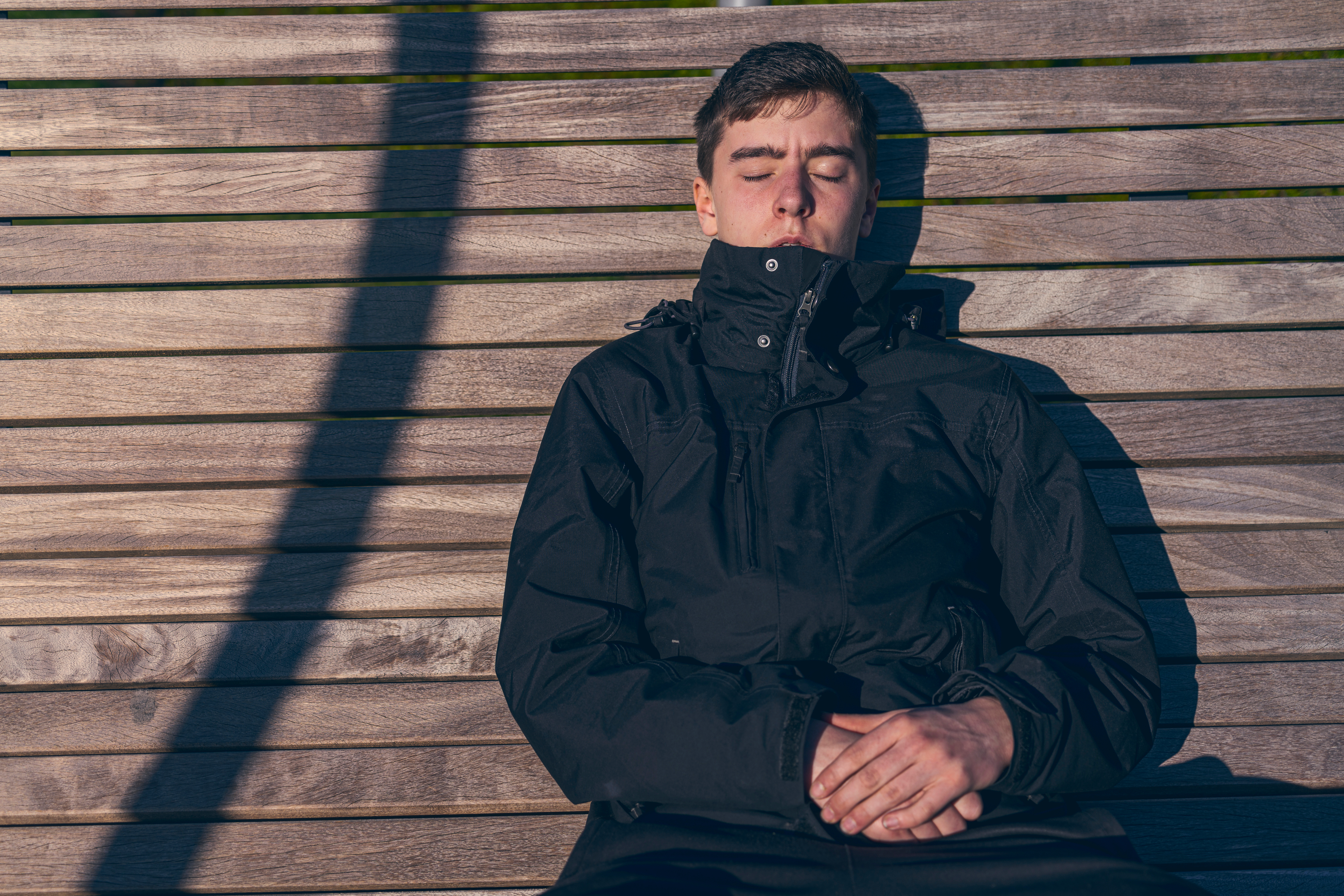 Young man sitting on a bench in the sun with his eyes closed | Source: Shutterstock