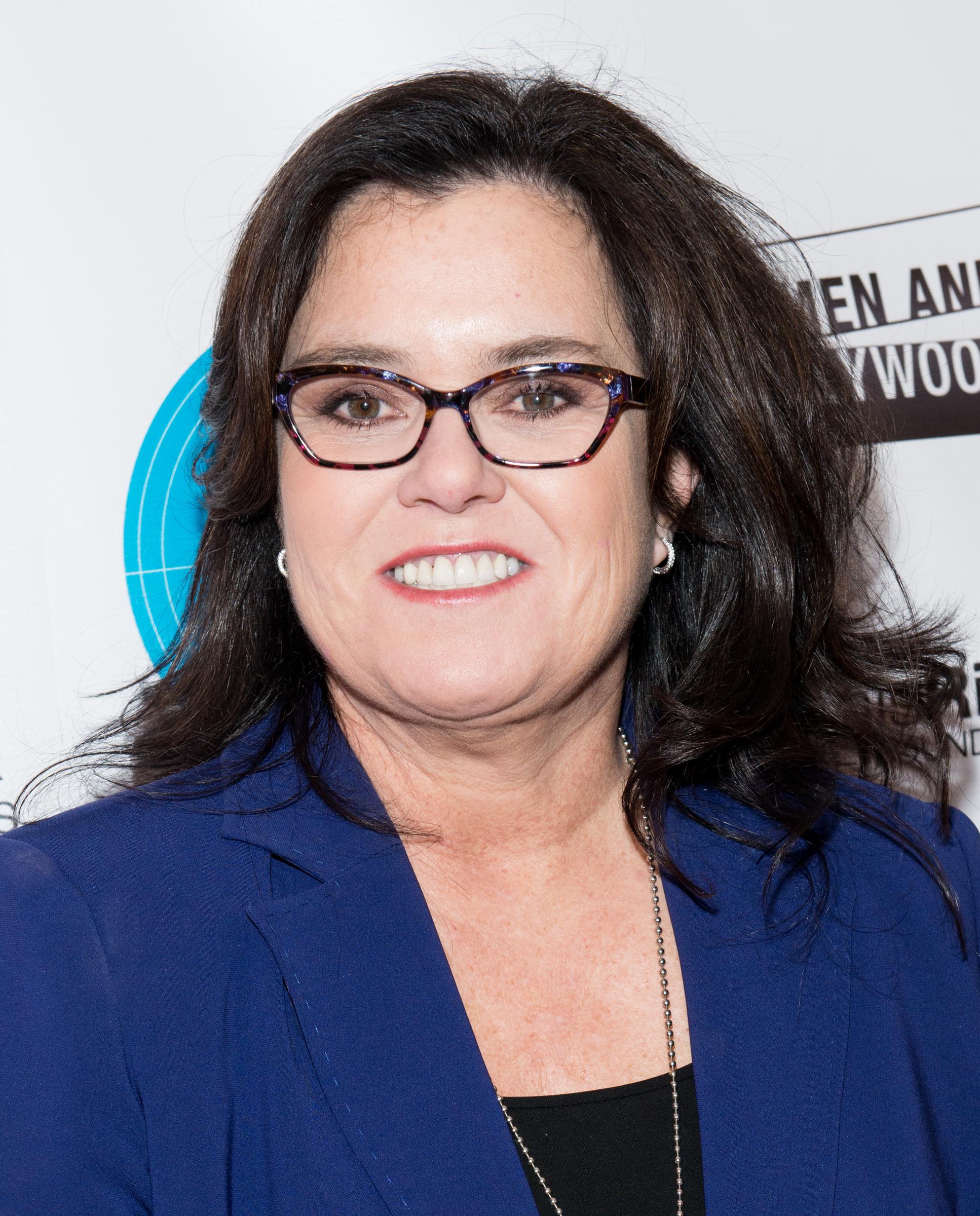 Rosie O'Donnell attends the Athena Film Festival Awards Ceremony at Barnard College in New York City, smiling on the red carpet in a royal blue blazer and patterned eyeglasses.
