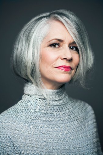Femme mûre aux cheveux gris argenté devant un fond gris foncé, portant du rouge à lèvres rouge avec un sourire doux, portrait. | Photo : Getty Images