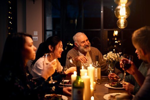 Cheerful guests at dinner table listening to friend and drinking wine | Photo: Getty Images