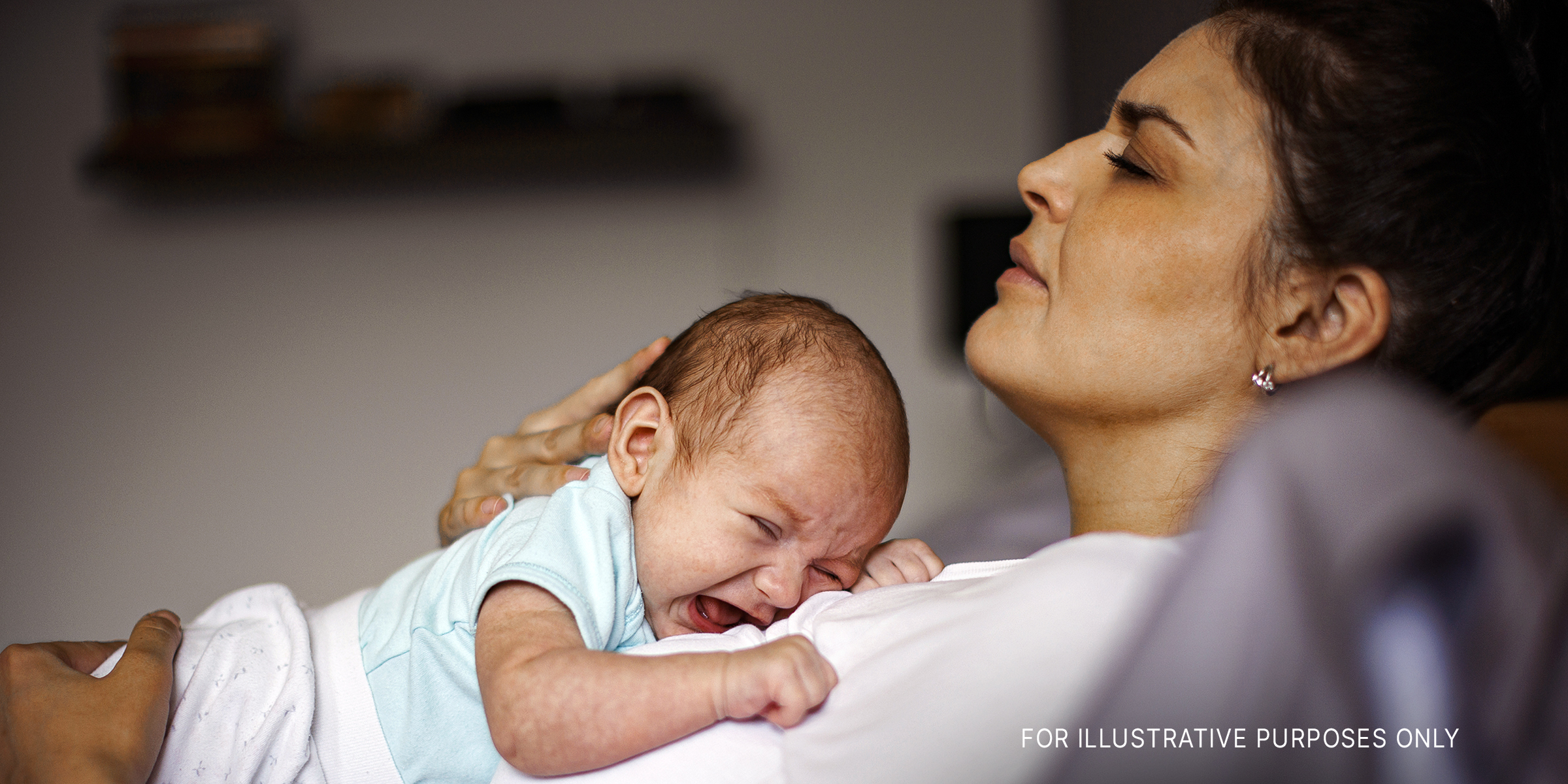 A distressed woman laying down with her crying baby on her chest | Source: Getty Images
