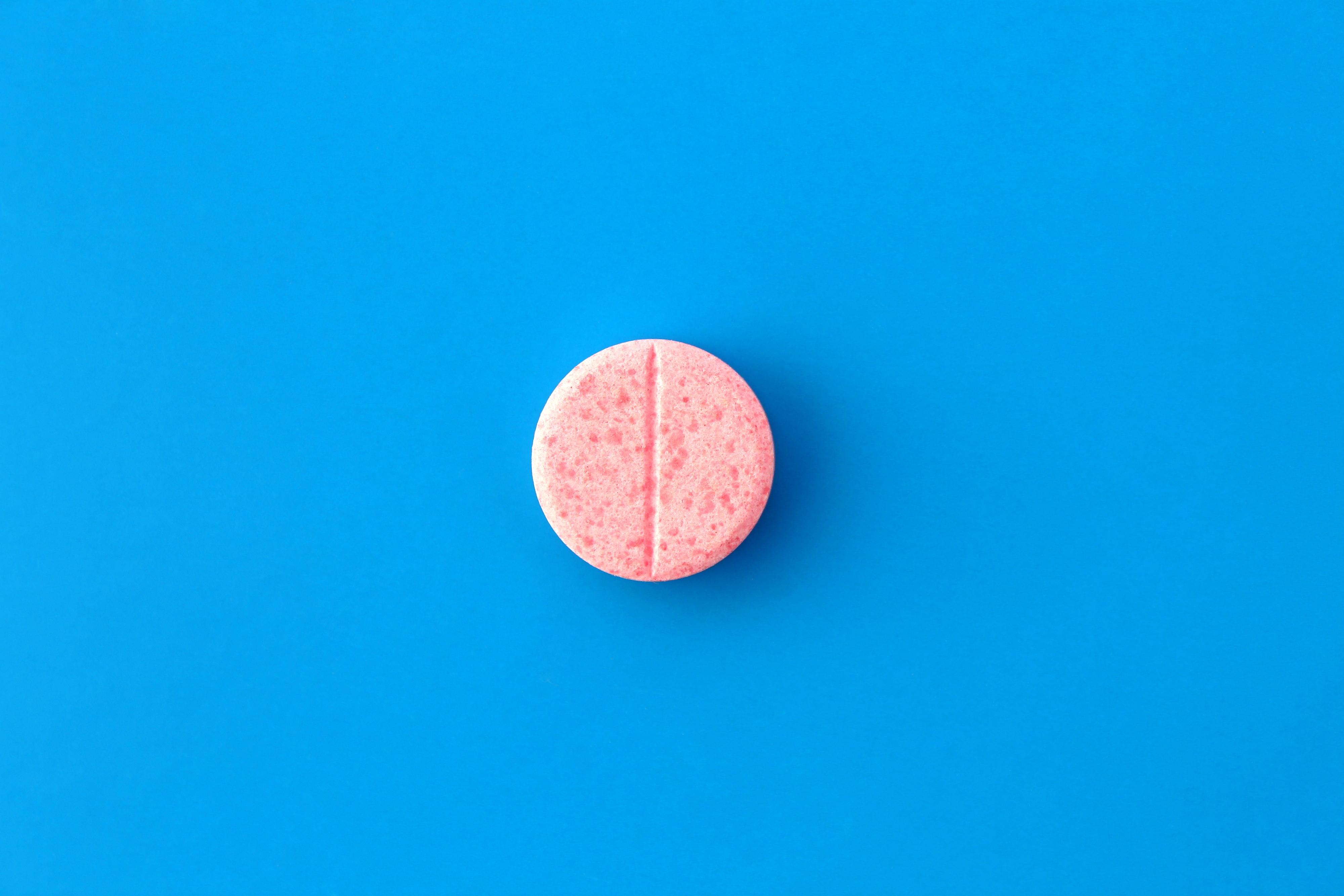 One pink pill lies on a blue background. | Source: Shutterstock
