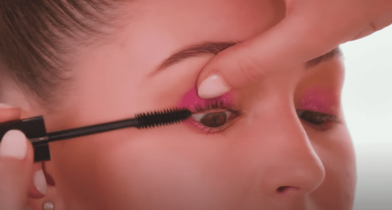 Makeup artist Caitilin Wyman applies mascara on a model's eyelashes. | Source: YouTube/ScottBarnes