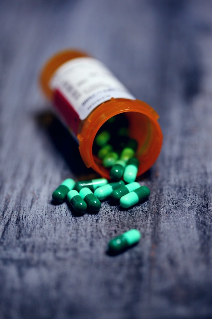 Recipiente de medicamentos abierto y las capsulas esparcidas en la mesa. | Foto: Unsplash