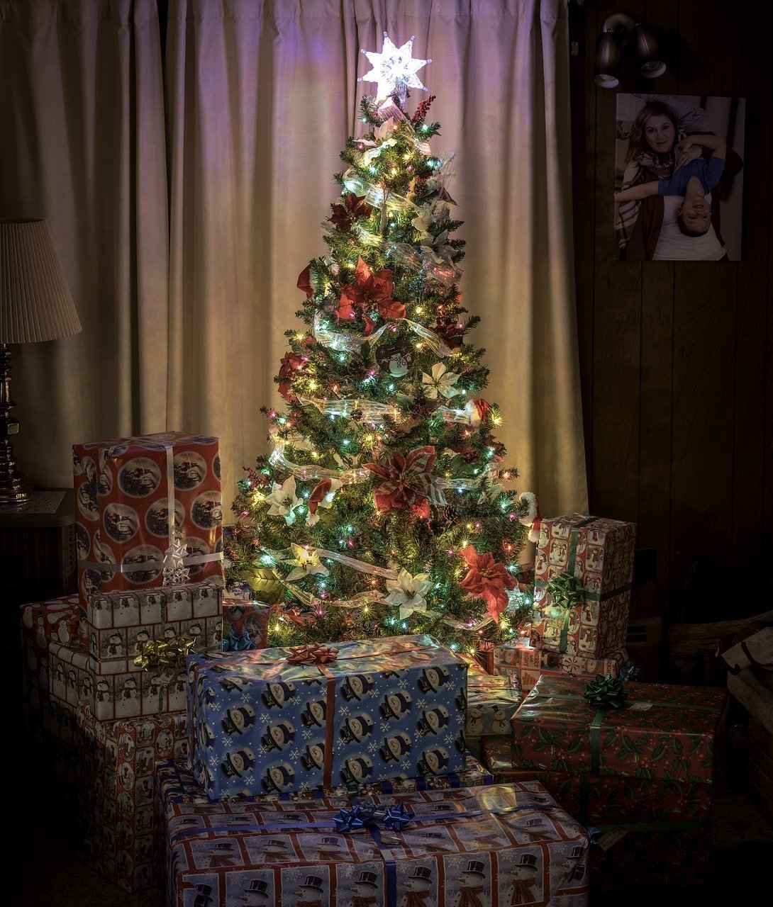 A fully-decorated Christmas tree in a dim-lit home's living room, with presents under it. | Photo: Pixabay.