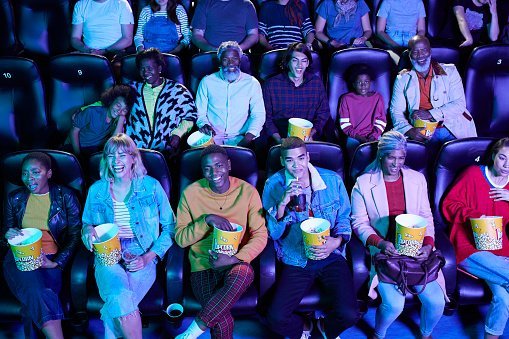 Photo of multi-ethnic audience enjoying popcorn while watching comedy movie at cinema hall | Photo: Getty Images