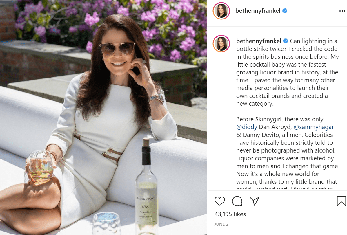 Pictured - Bethenny Frankel poses outdoors on a sunny day in a white dress sipping on her cocktail liquor brand | Source: Instagram/@bethennyfrankel