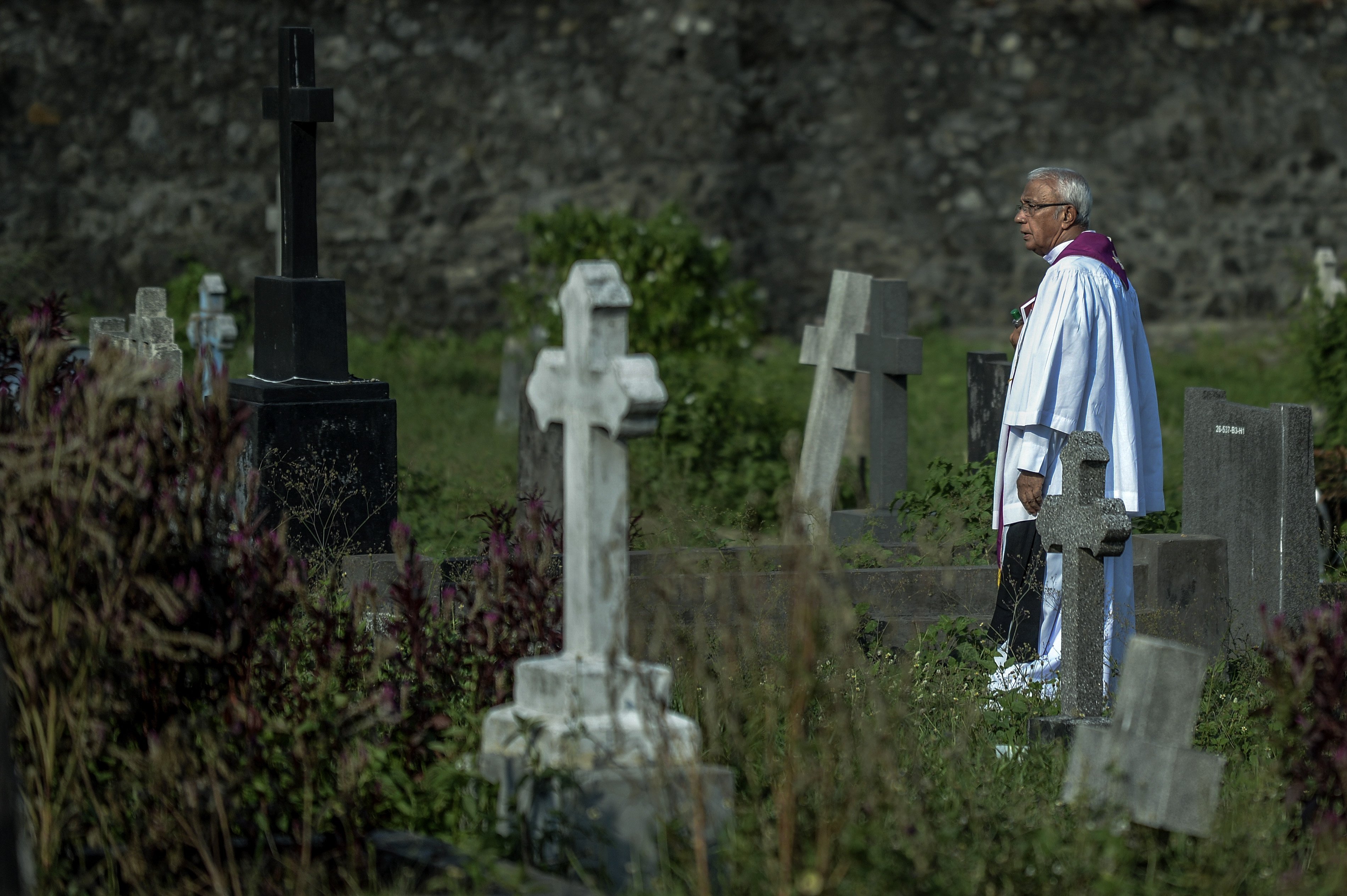  A priest waiting among the graves for the beginning of the burial of a victim of the Easter Sunday Bombings in Colombo, Sri Lanka | Photo: Getty Images