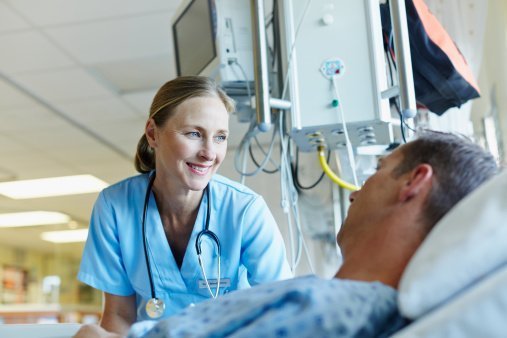 Happy female doctor conversing with male patient lying in hospital ward | Photo: Getty Images