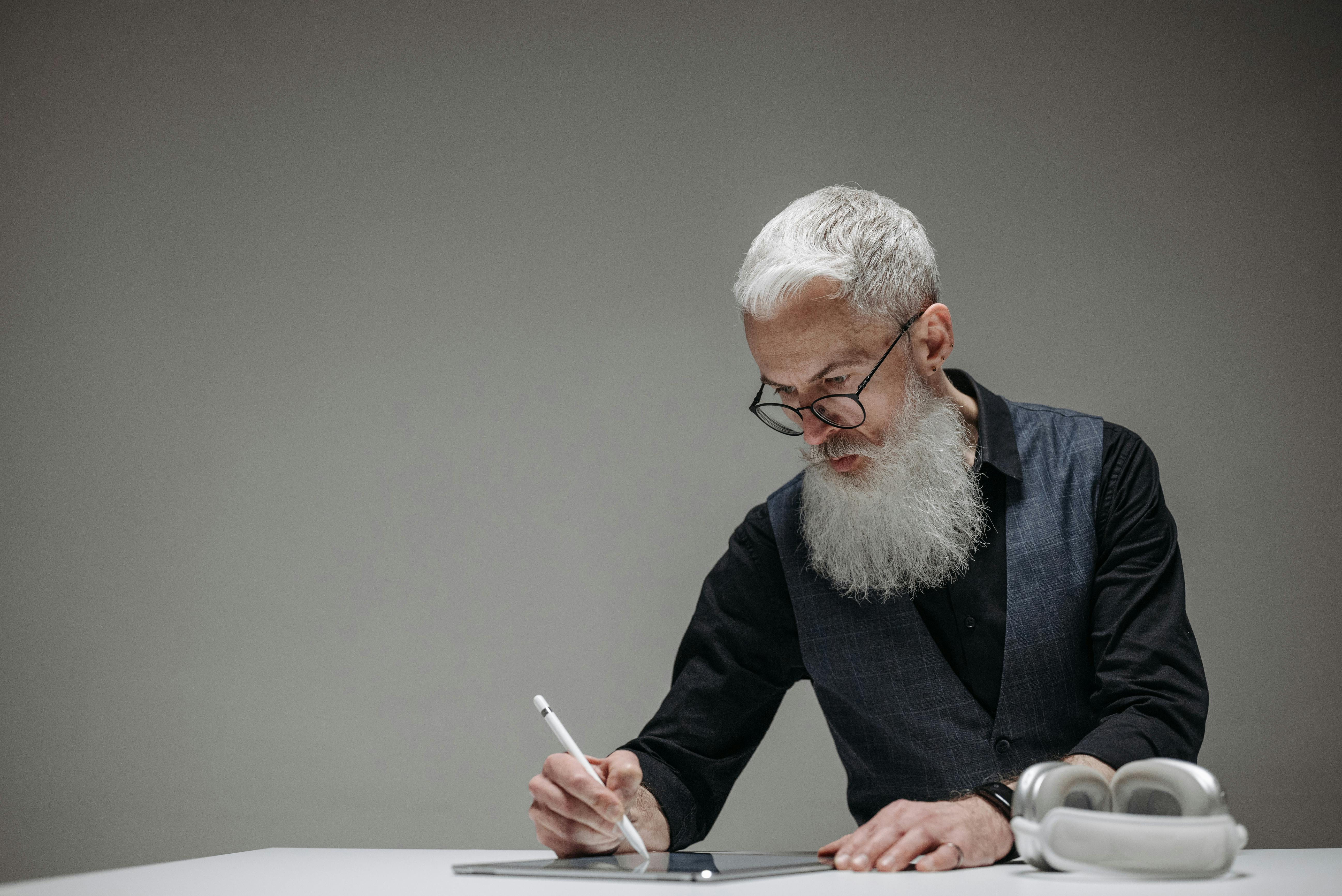 Bearded man using a light pen on a tablet | Source: Pexels