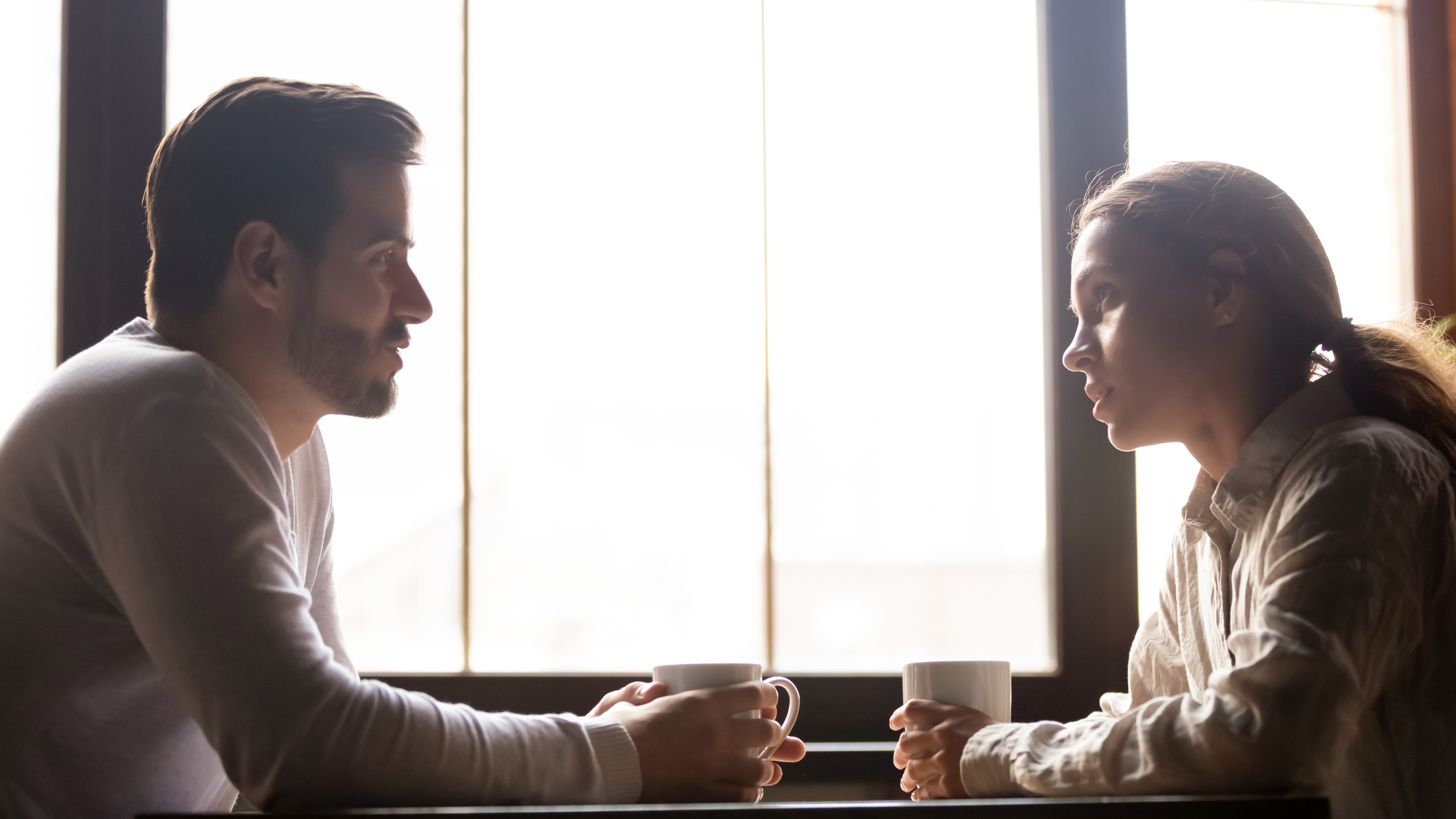 A man and woman sitting across each other, each holding a cup | Source: Shutterstock
