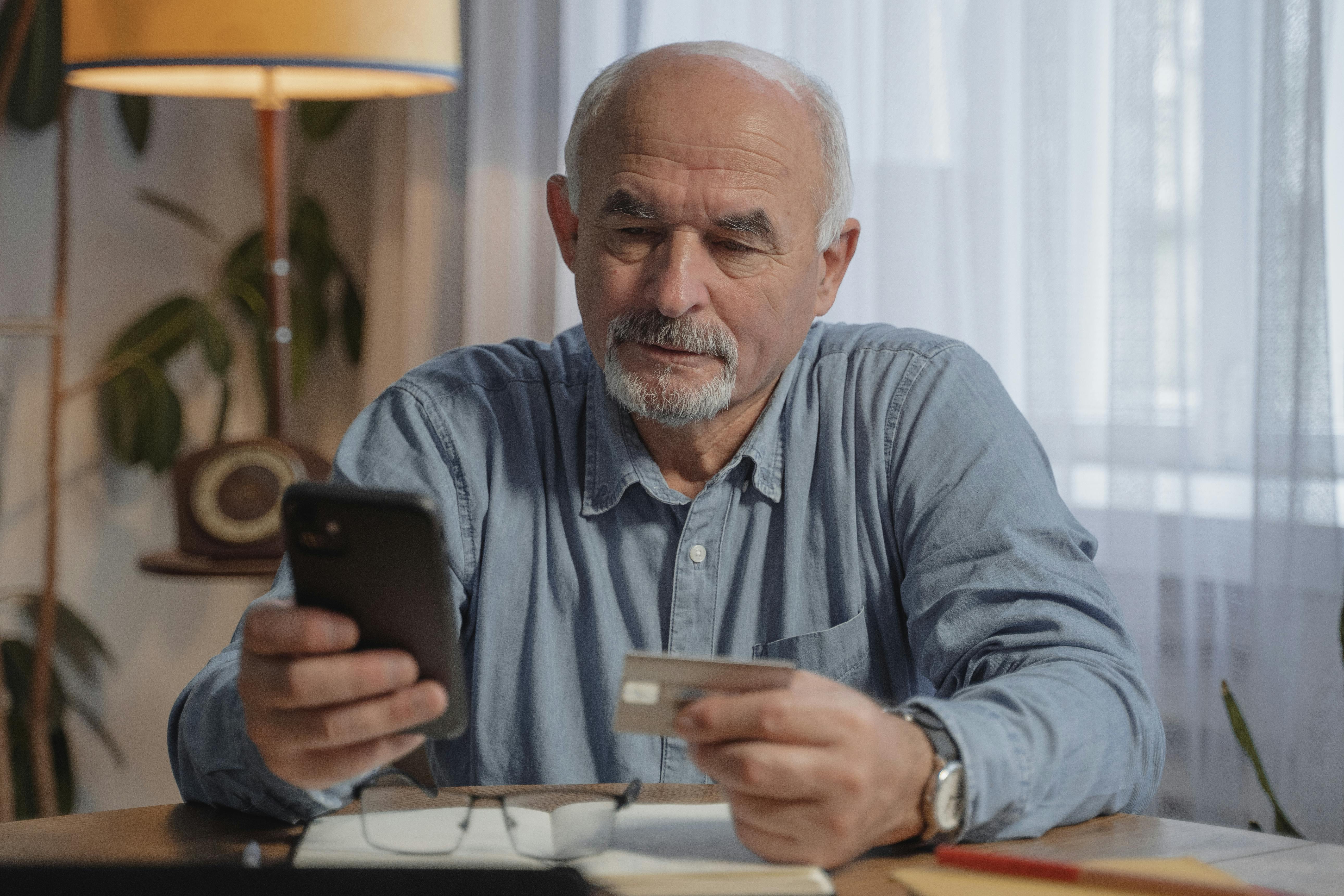 An older man holding his phone in one hand and a bank card in the other | Source: Pexels