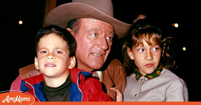 American actor John Wayne (1907 - 1979) with two of his children, son John Ethan and daughter Aissa Wayne, as they are photographed in an unspecified restaurant, 1967. Wayne is in costume (as Cole Thornton) for his role in 'El Dorado' | Source: Getty Images