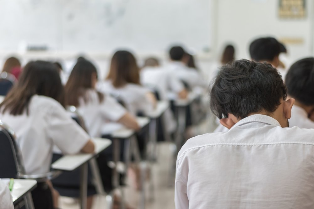 Blur photo of school students writing during an exam in the classroom. | Shutterstock