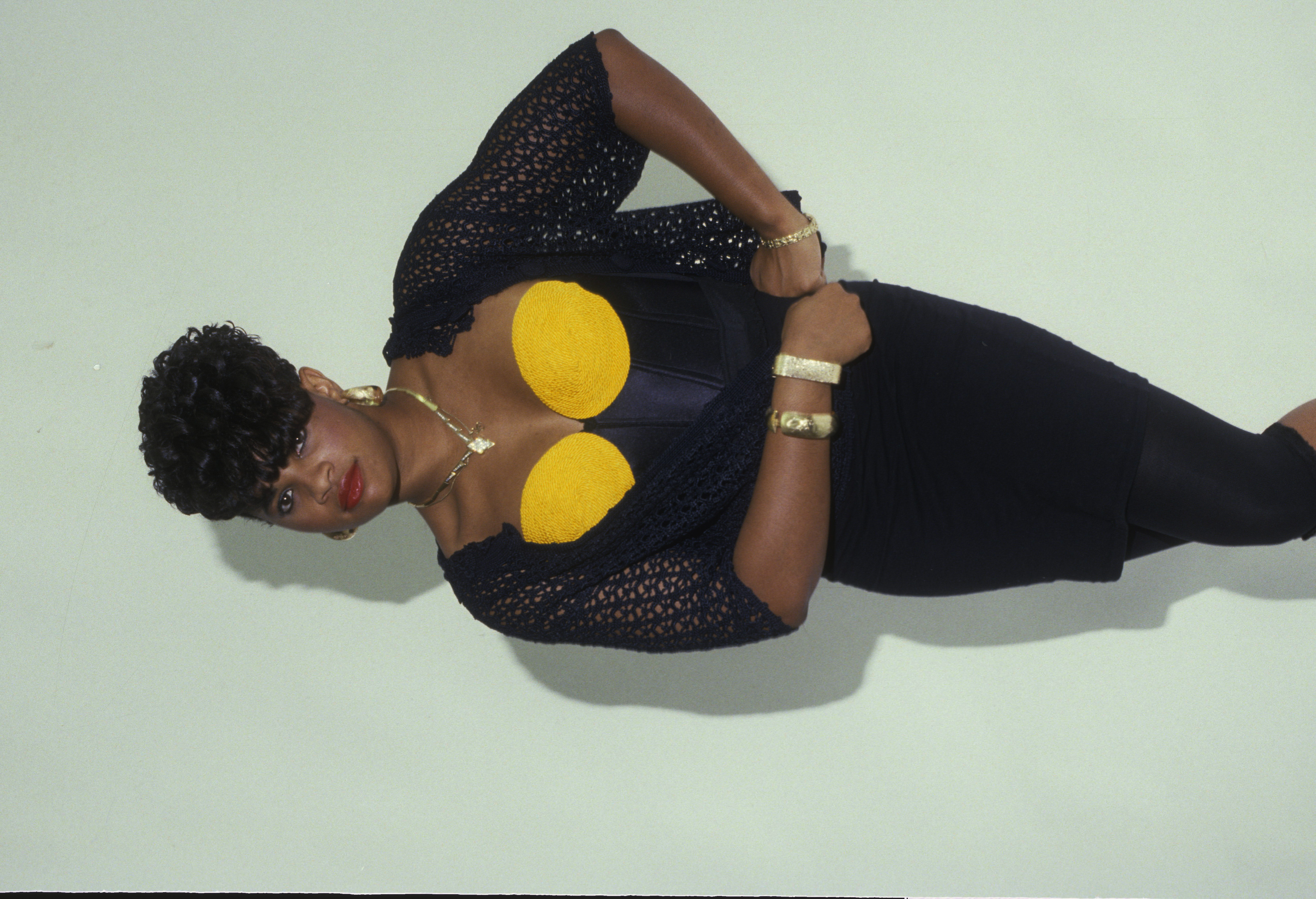 Sandy "Pepa" Denton strikes a bold pose in New York City. Her bright yellow bustier and gold jewelry radiate the era's pure hip-hop confidence. Her sculpted curls and bolder styling mark the beginning of her shift toward more dramatic beauty choices.