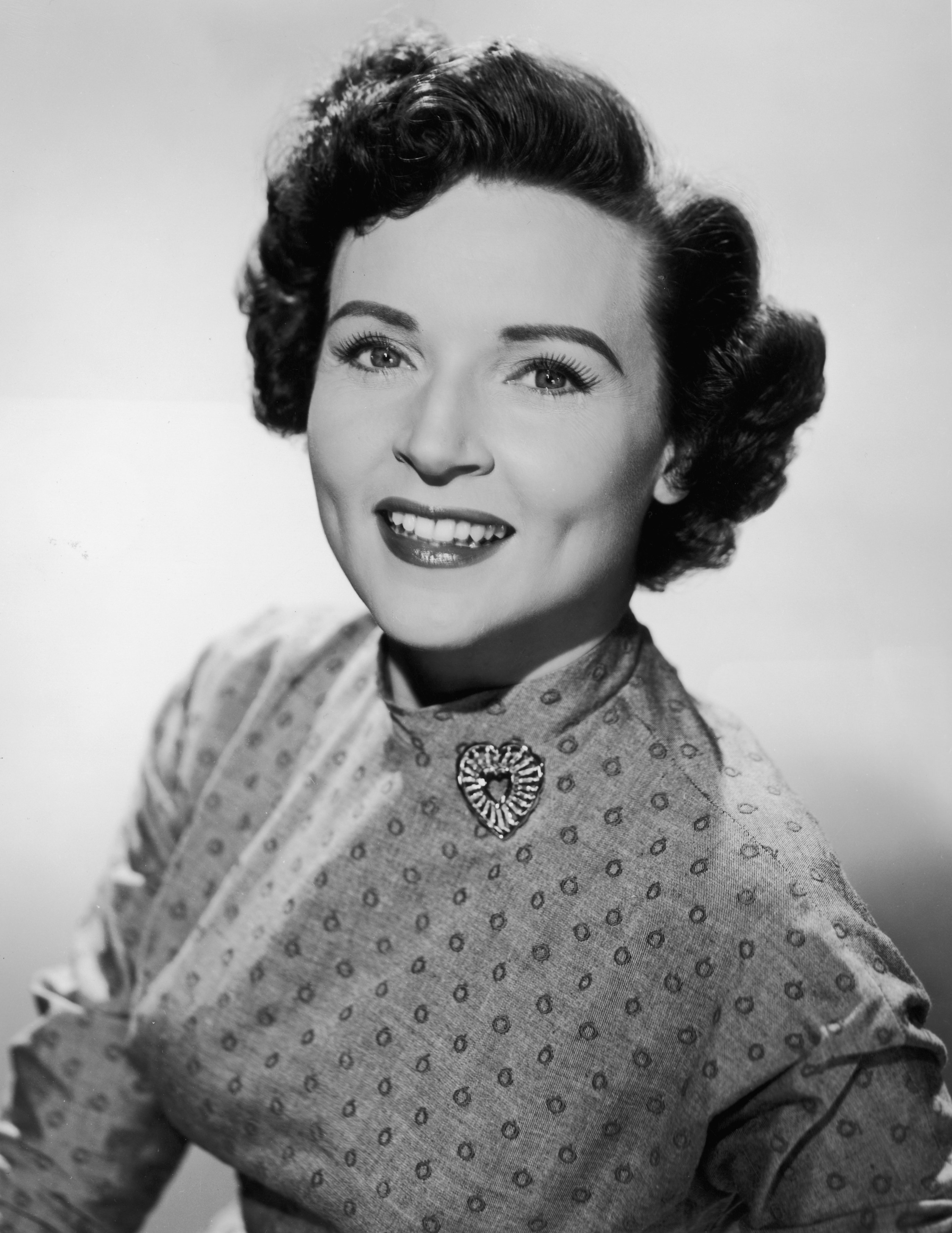 Ein Studioporträt der strahlenden Schauspielerin Betty White in einem gemusterten Kleid mit herzförmiger Brosche im Jahr 1955 ┃ Quelle: Getty Images