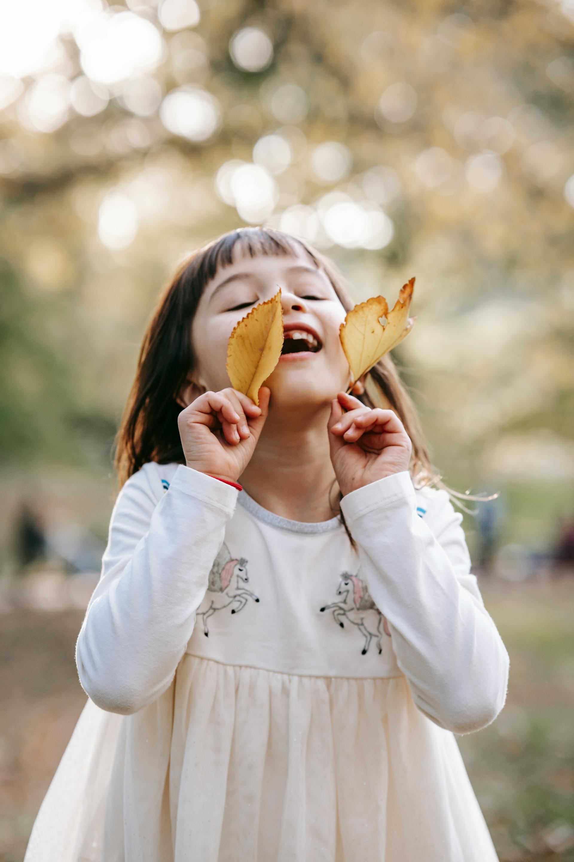 A happy little girl with yellow leaves standing in a park | Source: Pexels
