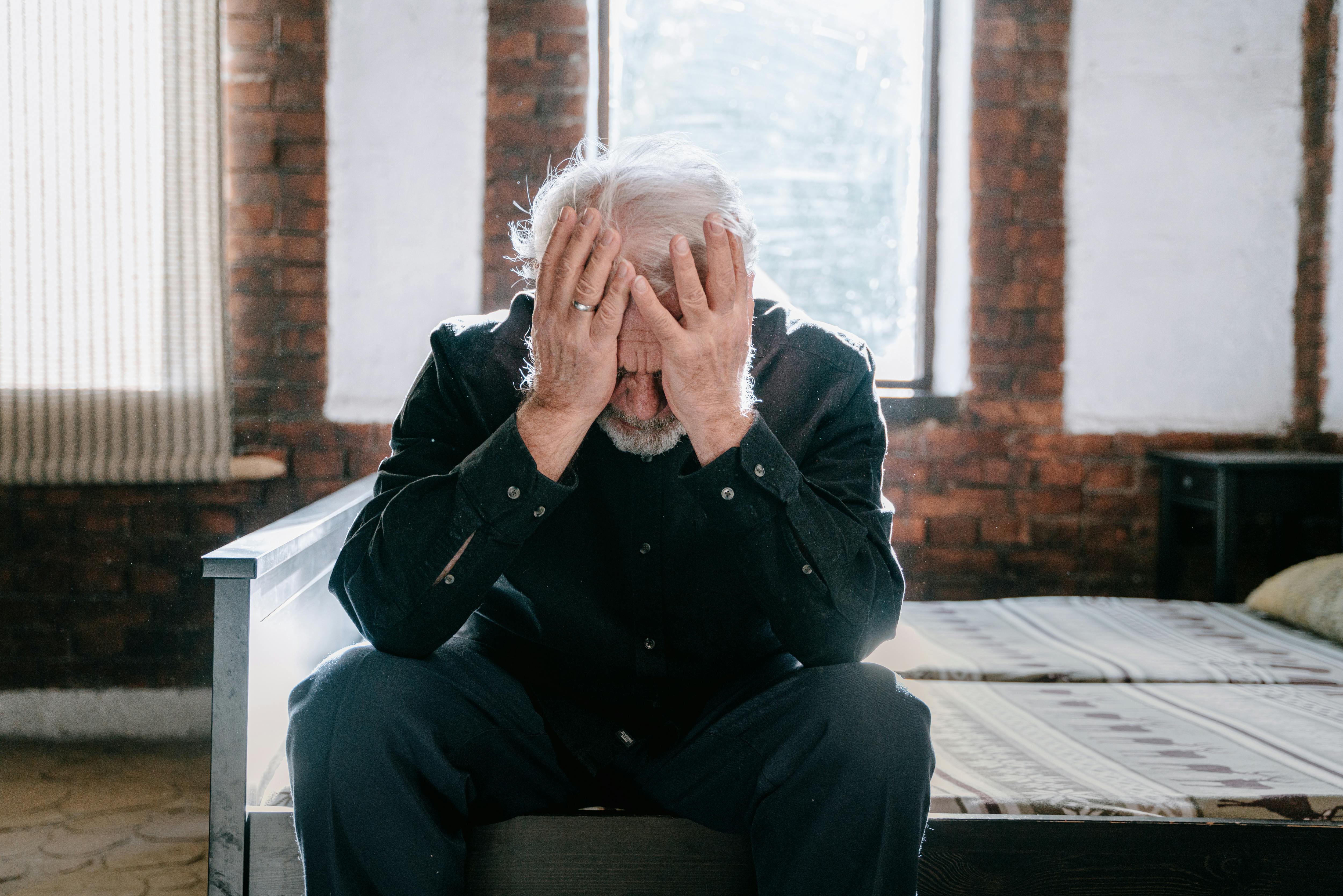 A distressed man sitting on a bed with his hands covering his face | Source: Pexels