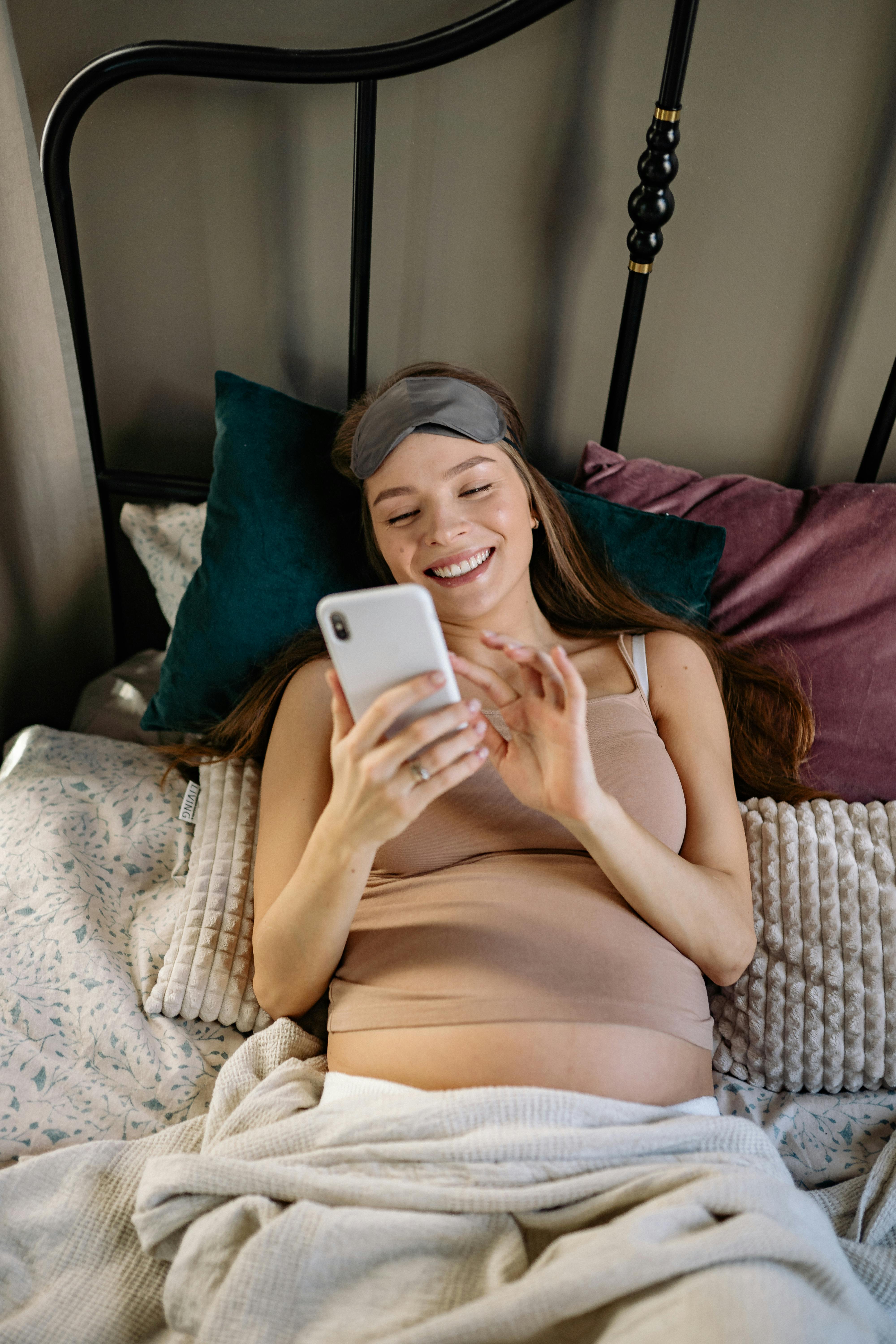 A smiling pregnant woman reading her phone in bed | Source: Pexels