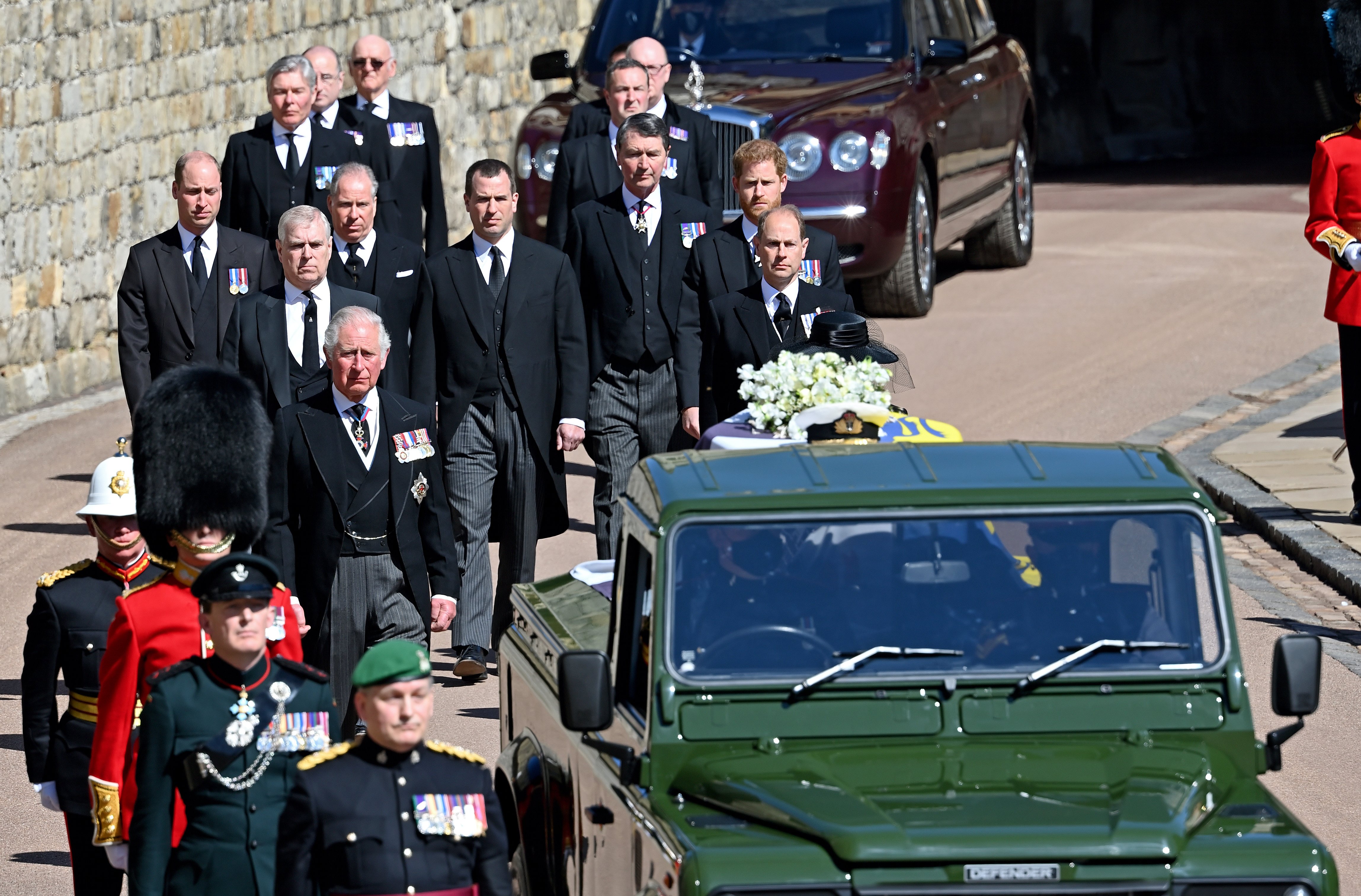 Prince Charles, Prince of Wales, Prince Andrew, Duke of York, Prince Edward, Earl of Wessex, Prince William, Duke of Cambridge, Peter Phillips, Prince Harry, Duke of Sussex, David Armstrong-Jones, 2nd Earl of Snowdon and Vice Admiral Sir Timothy Laurence follow Prince Philip, Duke of Edinburgh's coffin (draped in his Royal Standard Flag and bearing his Royal Navy cap, sword and a bouquet of lilies, white roses, freesia and sweet peas) as it is carried on a specially designed Land Rover Defender hearse during his funeral procession to St. George's Chapel, Windsor Castle on April 17, 2021. | Source: Getty Images 