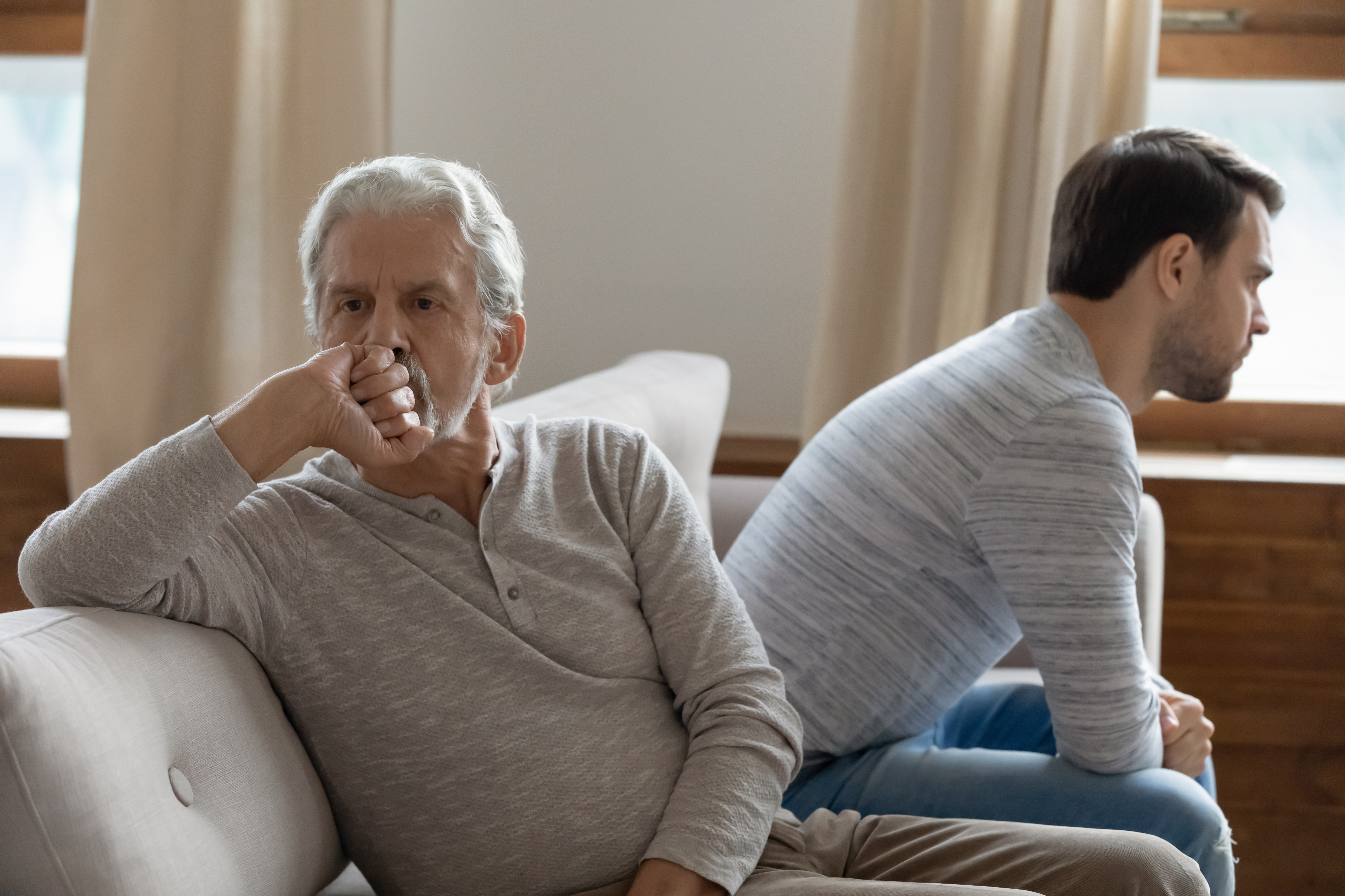 An unhappy older man sitting facing away from a younger one | Source: Shutterstock