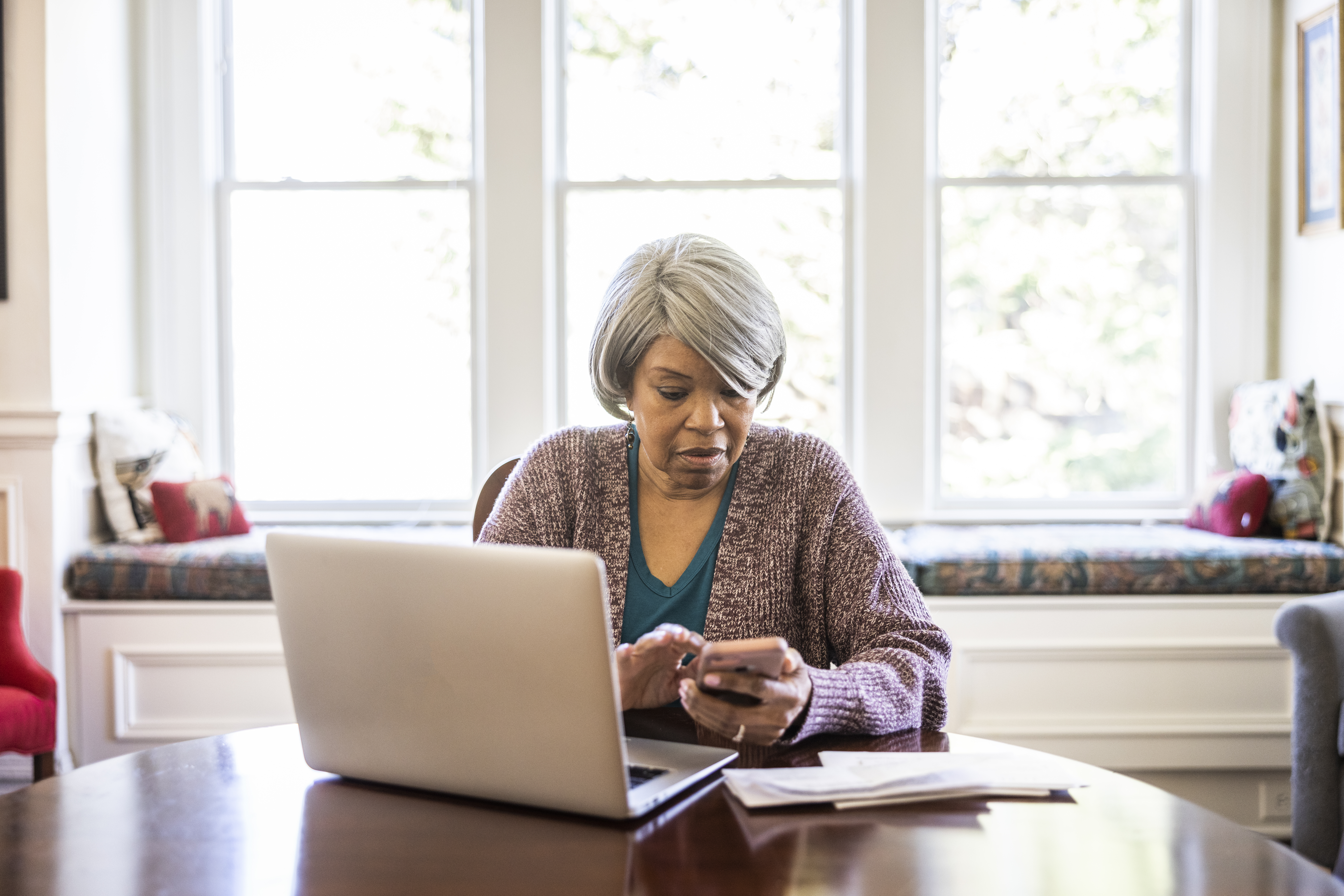 Senior woman paying bills with laptop and smartphone at home | Source: Getty Images