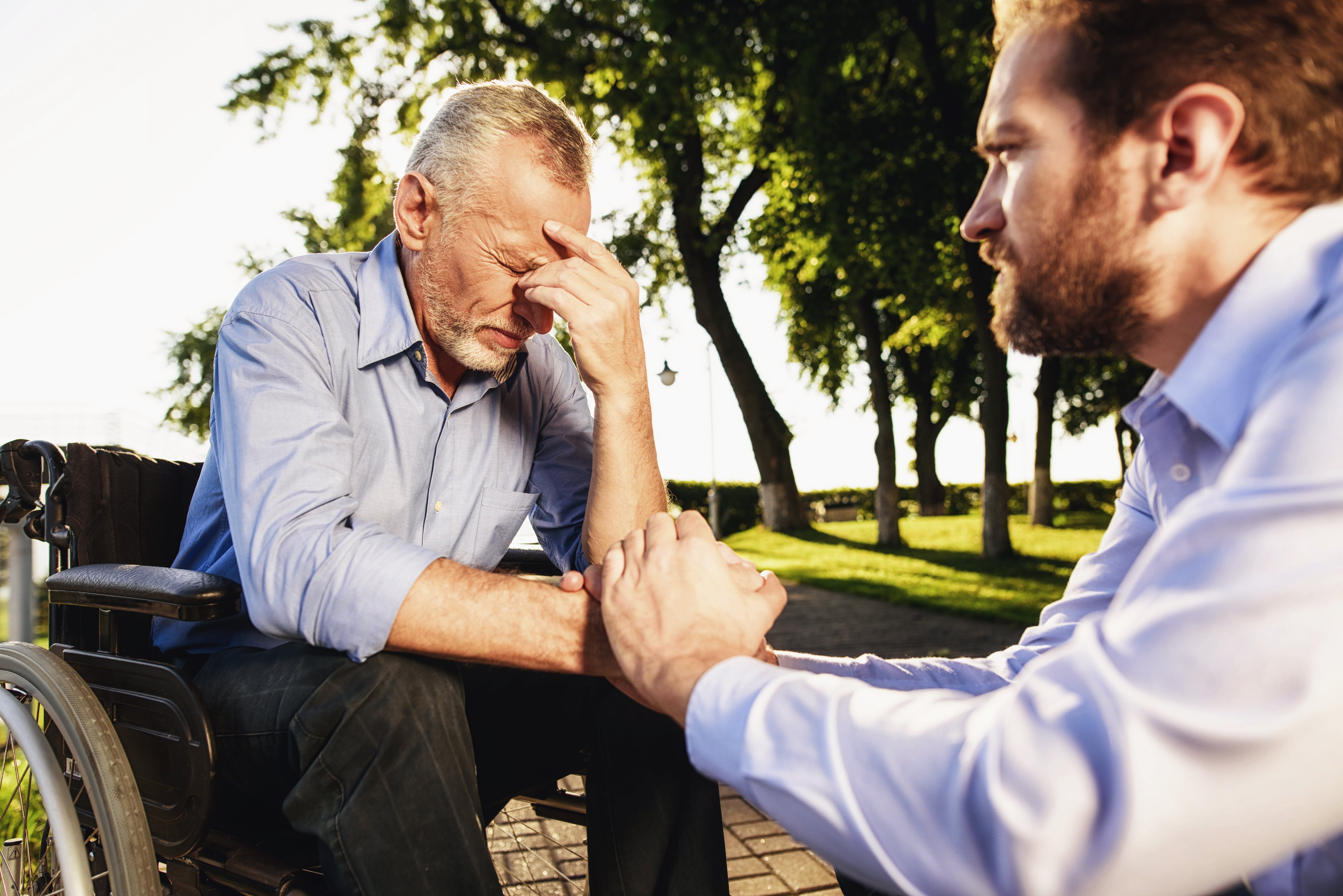 A young man is crouched next to an old man, who is thinking hard | Photo: Shutterstock.com