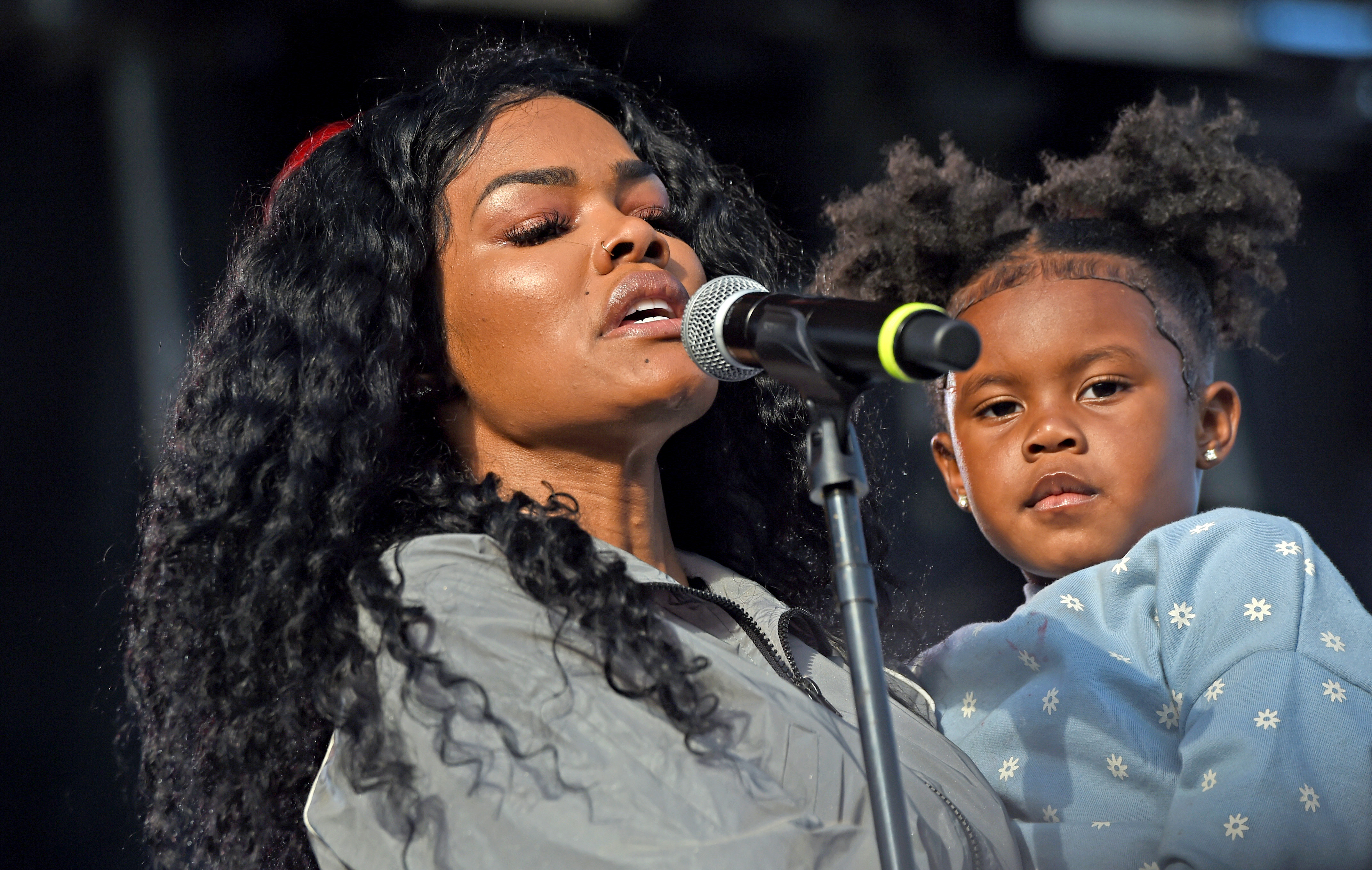 Teyana Taylor performs at Dave Chappelle's Block Party in Dayton while holding Iman Tayla "Junie" Shumpert Jr. near the microphone. Junie looks toward the crowd as her mother sings onstage.