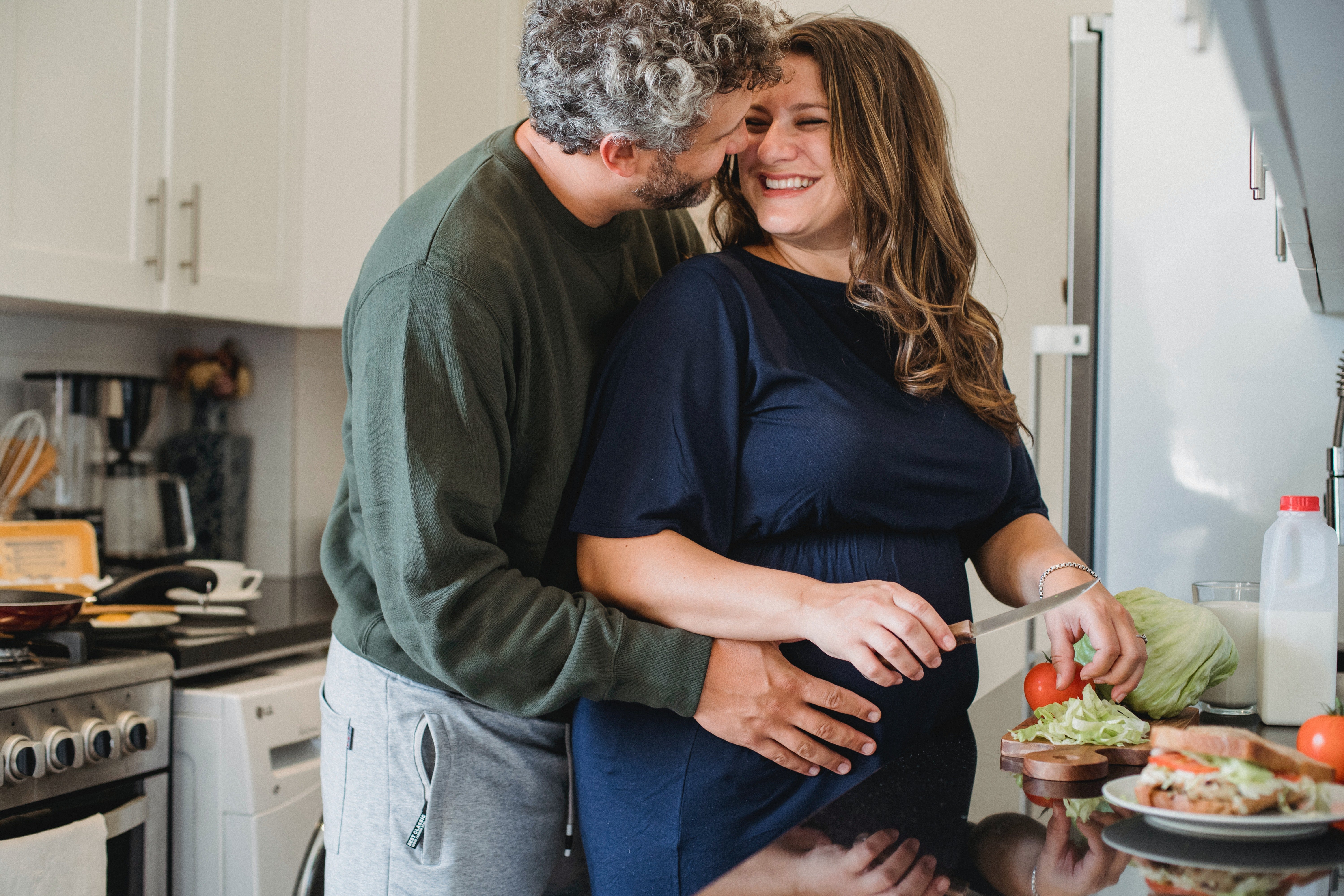A husband lovingly embracing his pregnant wife while she’s cooking. | Photo: Pexels/Amina Philkins