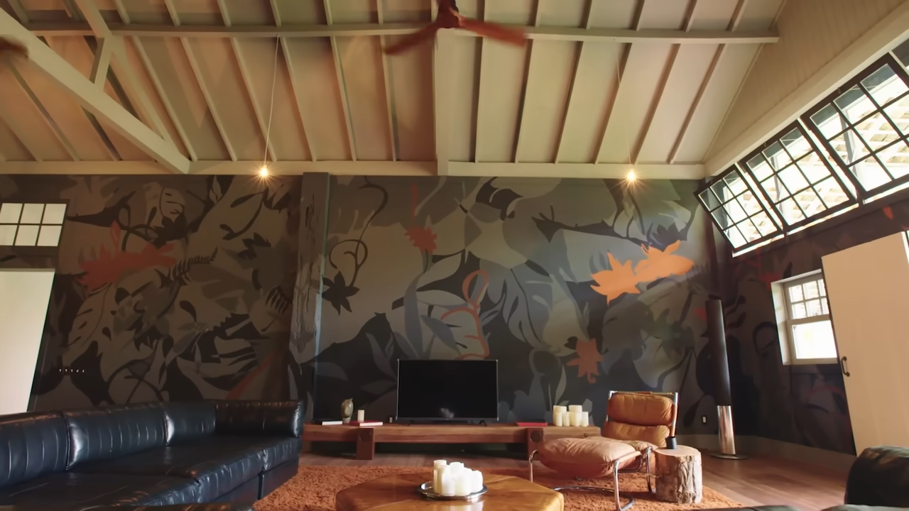 The expansive common area highlights an architectural cathedral ceiling with exposed wood trusses and matching dark wood ceiling fans. | Source: YouTube/@Archdigest