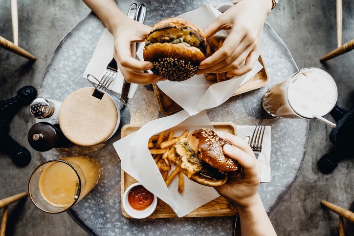 Friends having a good time eating burgers with french fries and drinks in a cafe | Photo: Getty Images