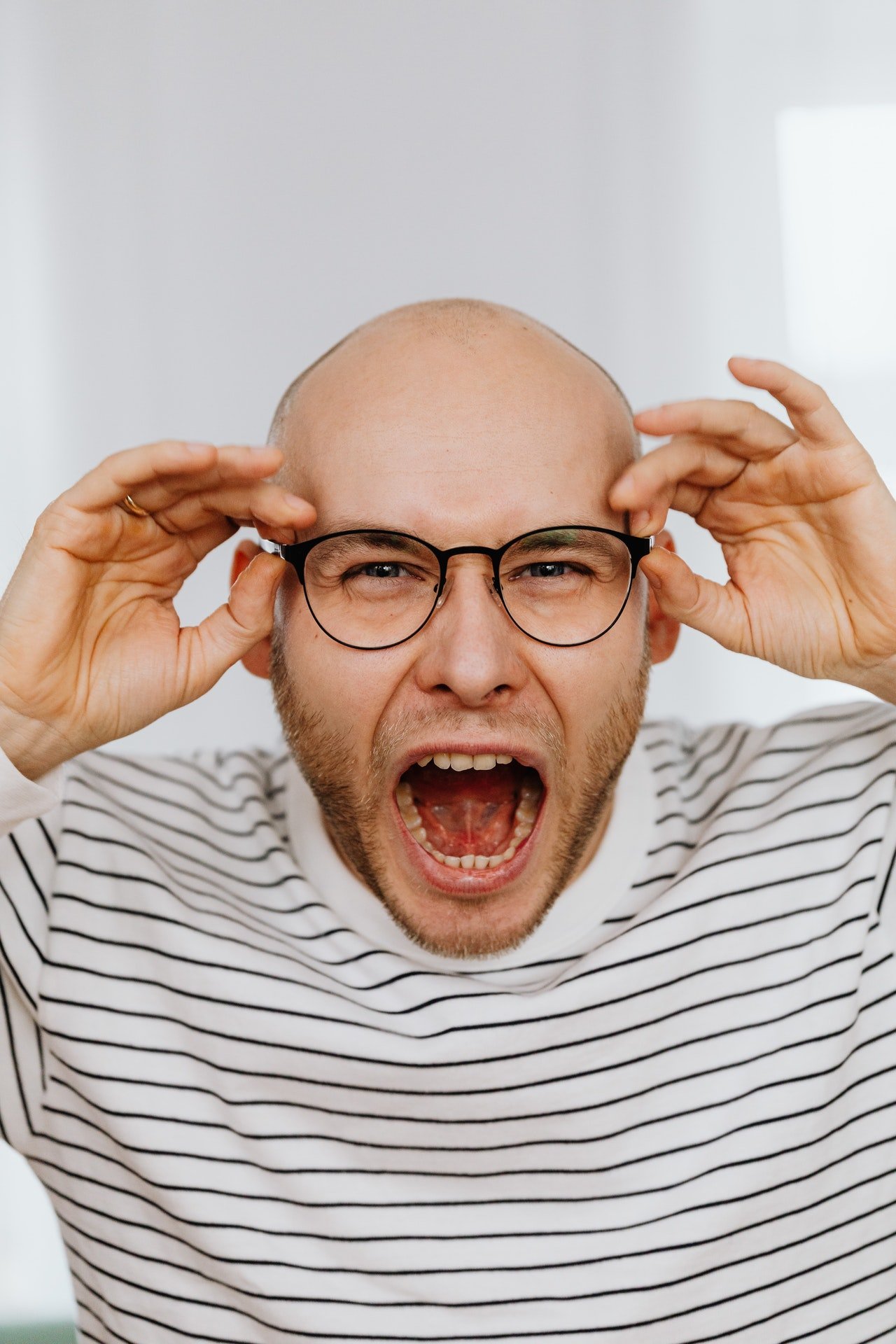 Hombre gritando mientras sostiene sus anteojos. | Foto: Pexels