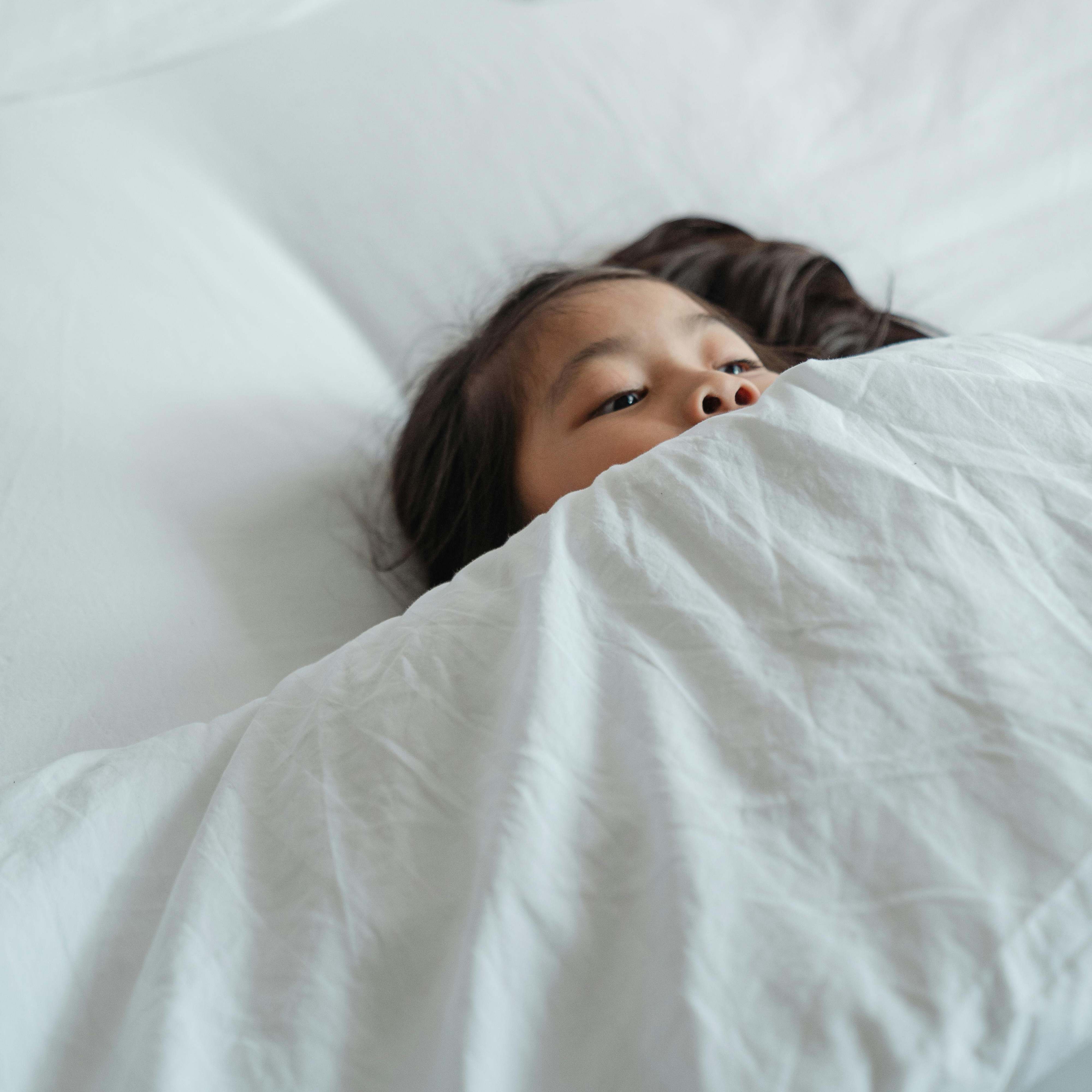 A young girl peeking above the bedcovers | Source: Pexels