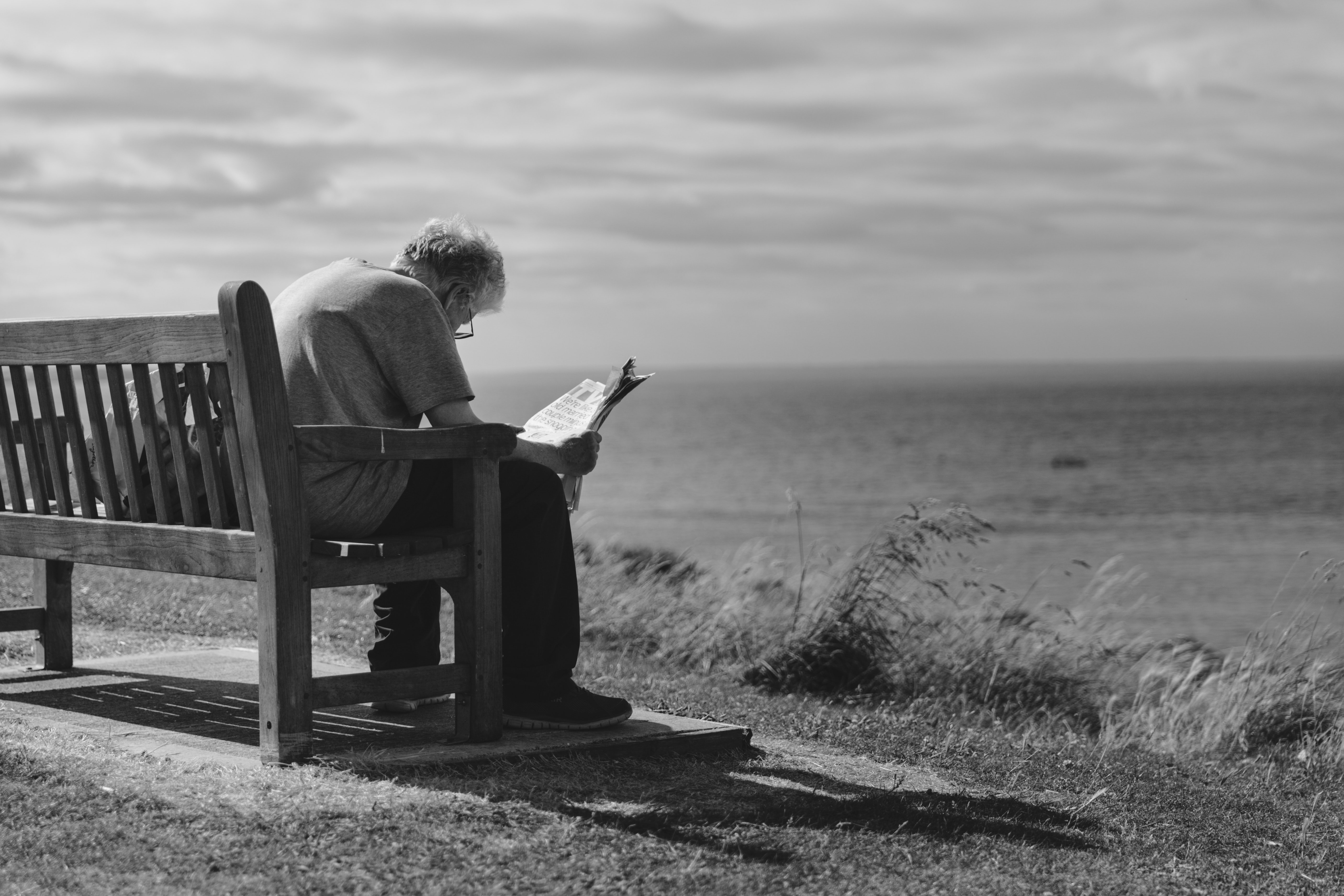 Hombre sentando en un banco leyendo el periódico. | Foto: Pexels