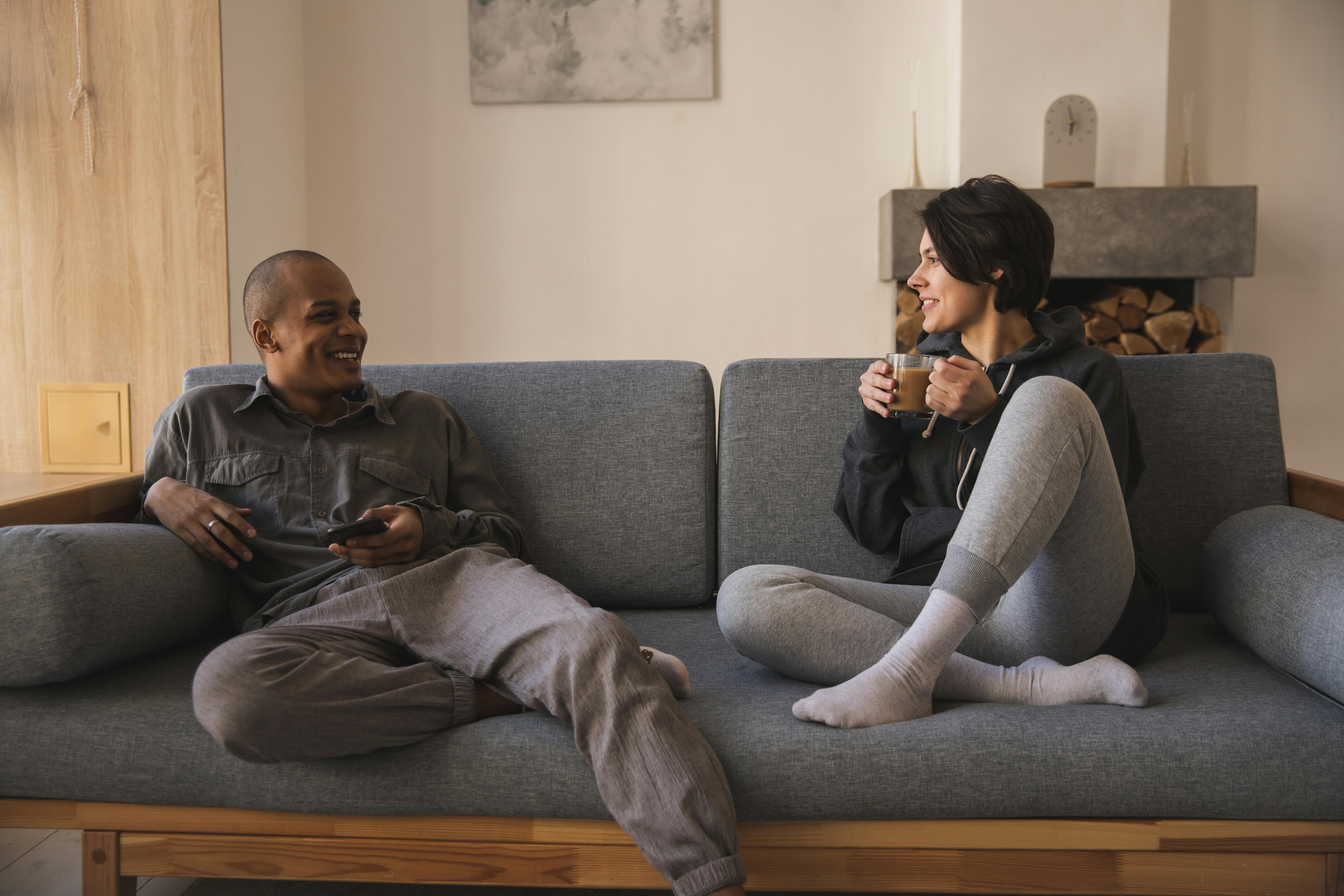A couple smiling while talking, seated on a couch | Source: Pexels