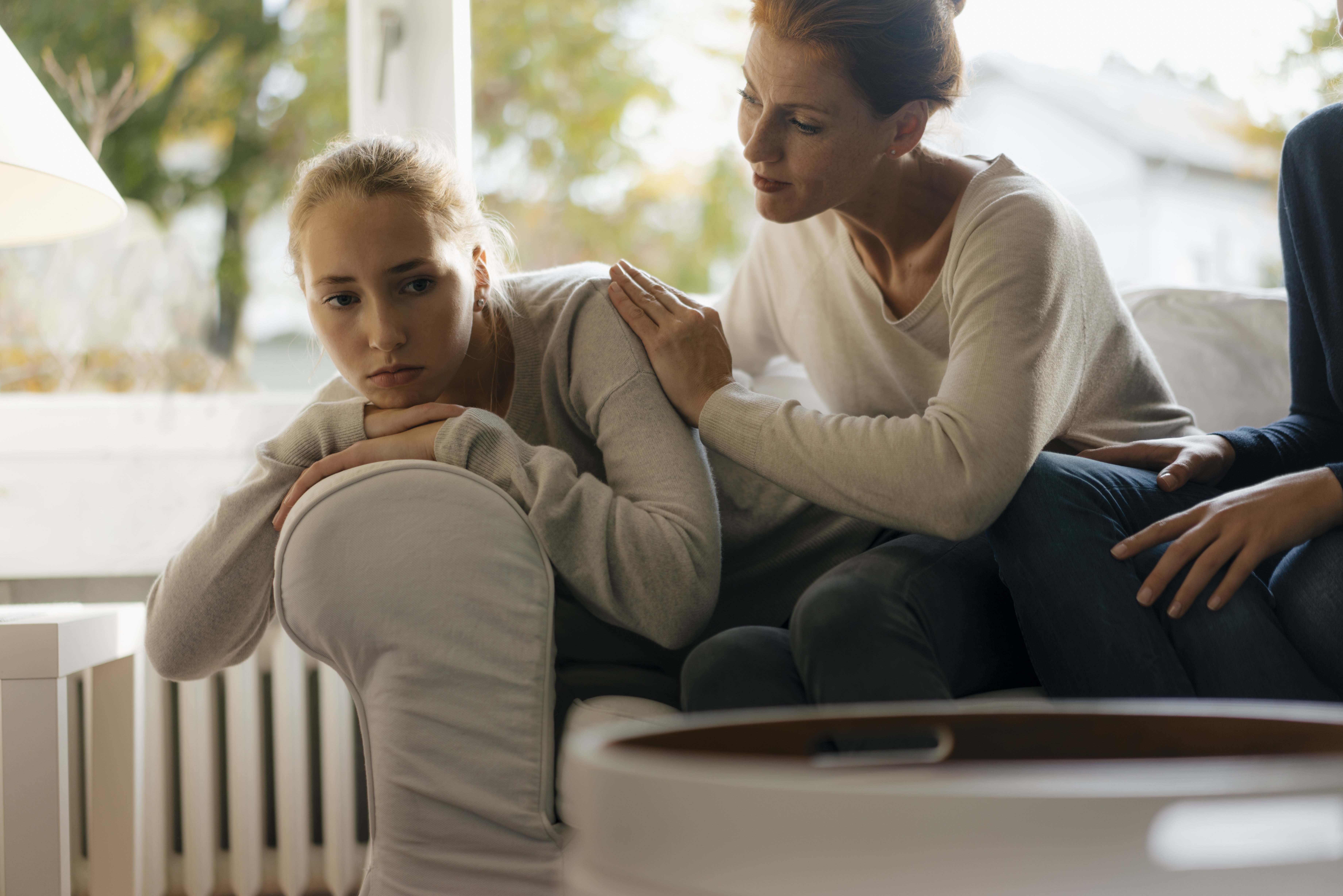 Mother consoling sad teenage girl on couch at home|Photo: Getty Images