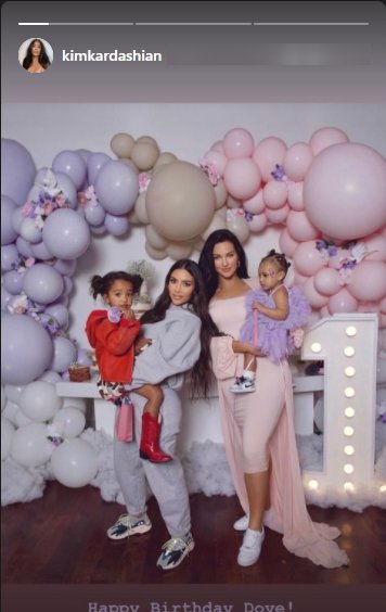 Kim Kardashian and Natalie Halcro hold their young daughters at Halcro’s daughter Dove’s party while posing for the camera together. | Source: Instagram/kimkardashian