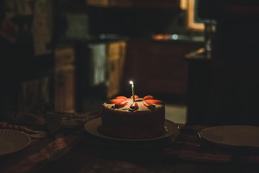 Photo of a round carrot cake  in a dark room with one lit birthday candle. | Photo: Getty Images