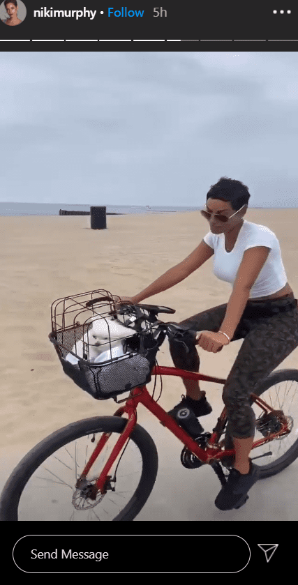 A photo of Nicole Murphy in a white T-shirt cycling with her puppy. | Photo: Instagram/Nikimurphy