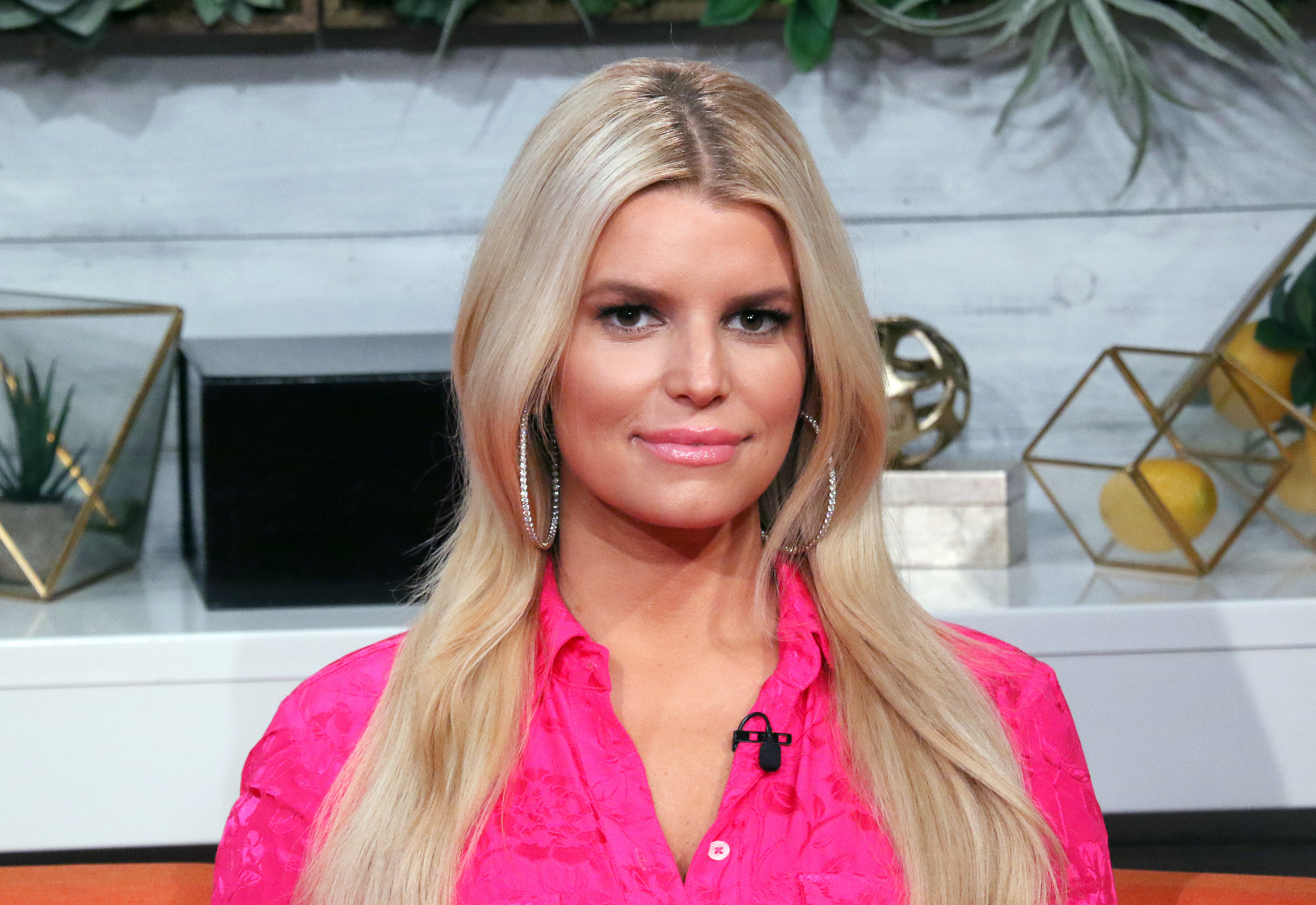 Jessica Simpson visited BuzzFeed's "AM to DM" in New York City. Wearing a hot pink blouse with straight blonde hair and hoop earrings, she embraced a sleek, professional look that contrasted with her earlier playful fashion.