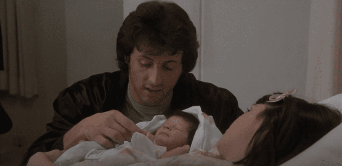 Sylvester Stallone as Rocky Balboa and Talia Shire as Adrian during a 1979 "Rocky II" scene with Stallone's newborn son Seargeoh Stallone. | Source: YouTube/Movieclips