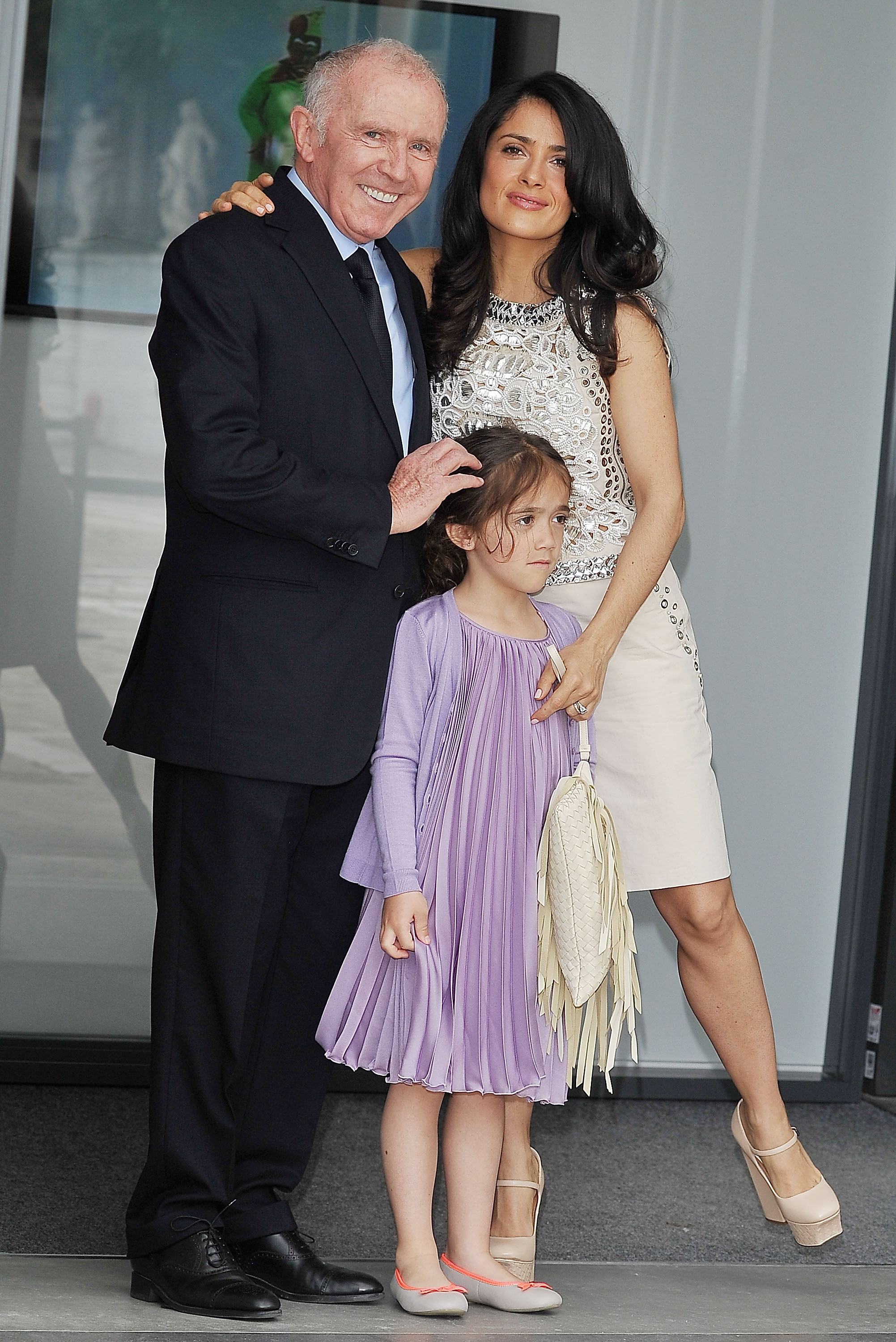At the VIP preview of "Prima Materia" in Venice, Salma Hayek poses alongside her father-in-law François Pinault, while Valentina Pinault stands at the center of the frame in a lilac pleated dress. The young girl appears serene while her mother — wearing a sleeveless embellished ivory dress — stands behind her.
