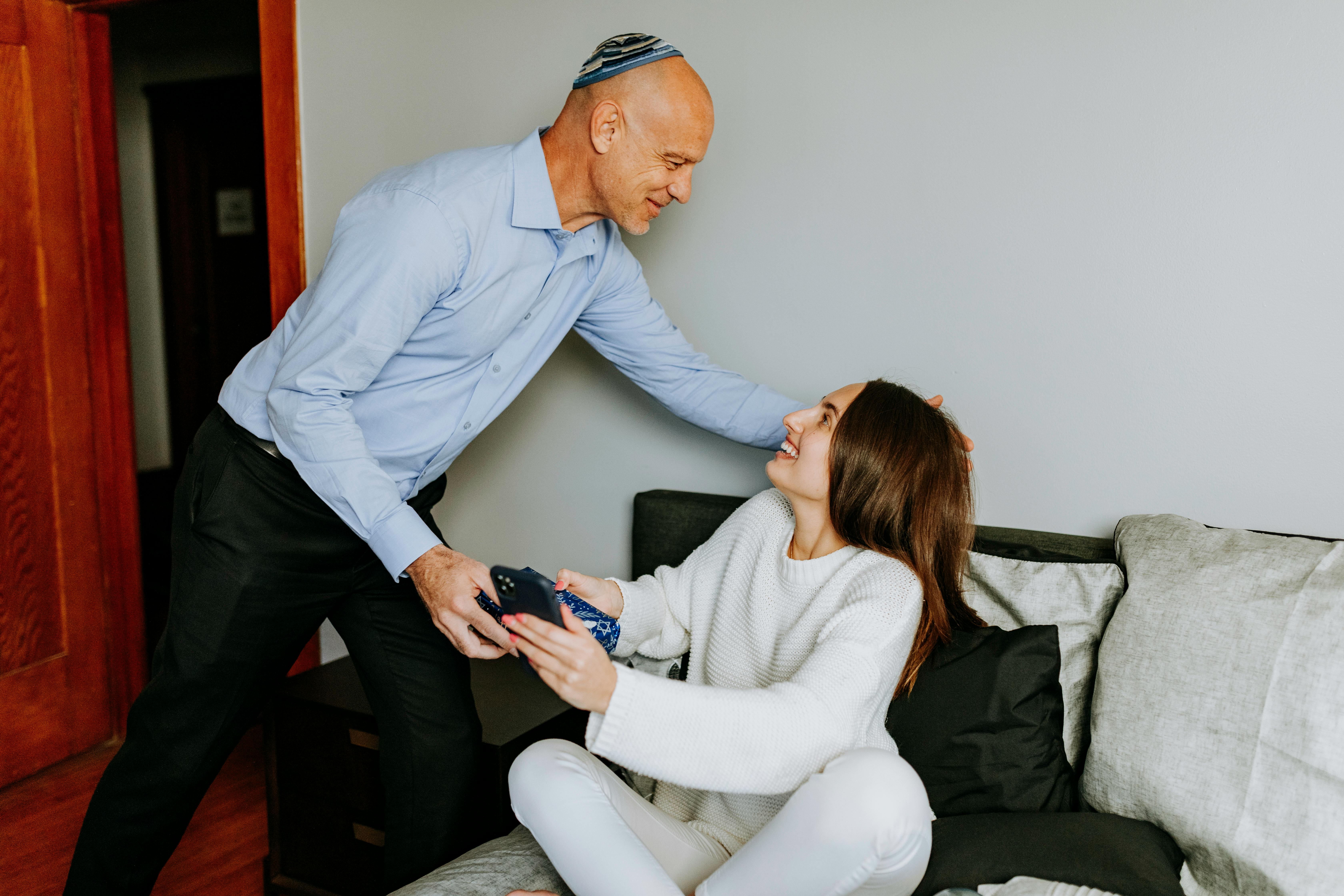 An older man reaching out to hug his daughter who's seated on a couch | Source: Pexels