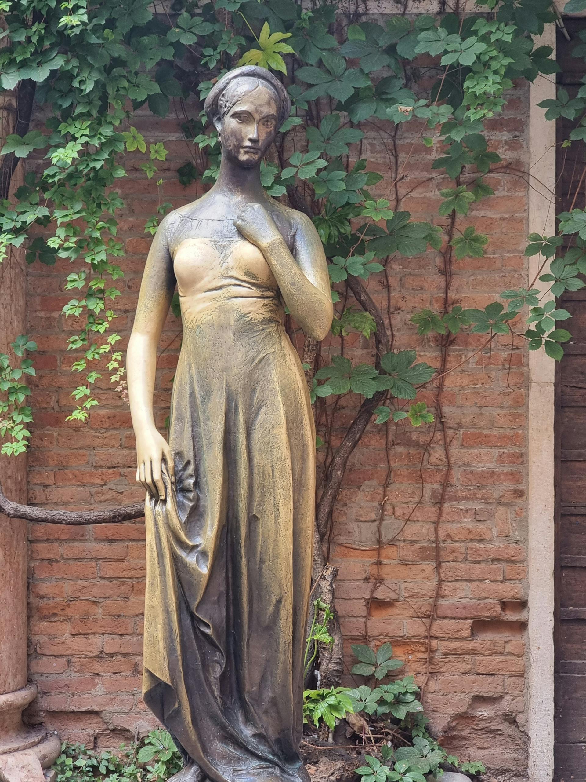 A metal statue of Juliet by a brick wall with a creeper plant | Source: Pexels