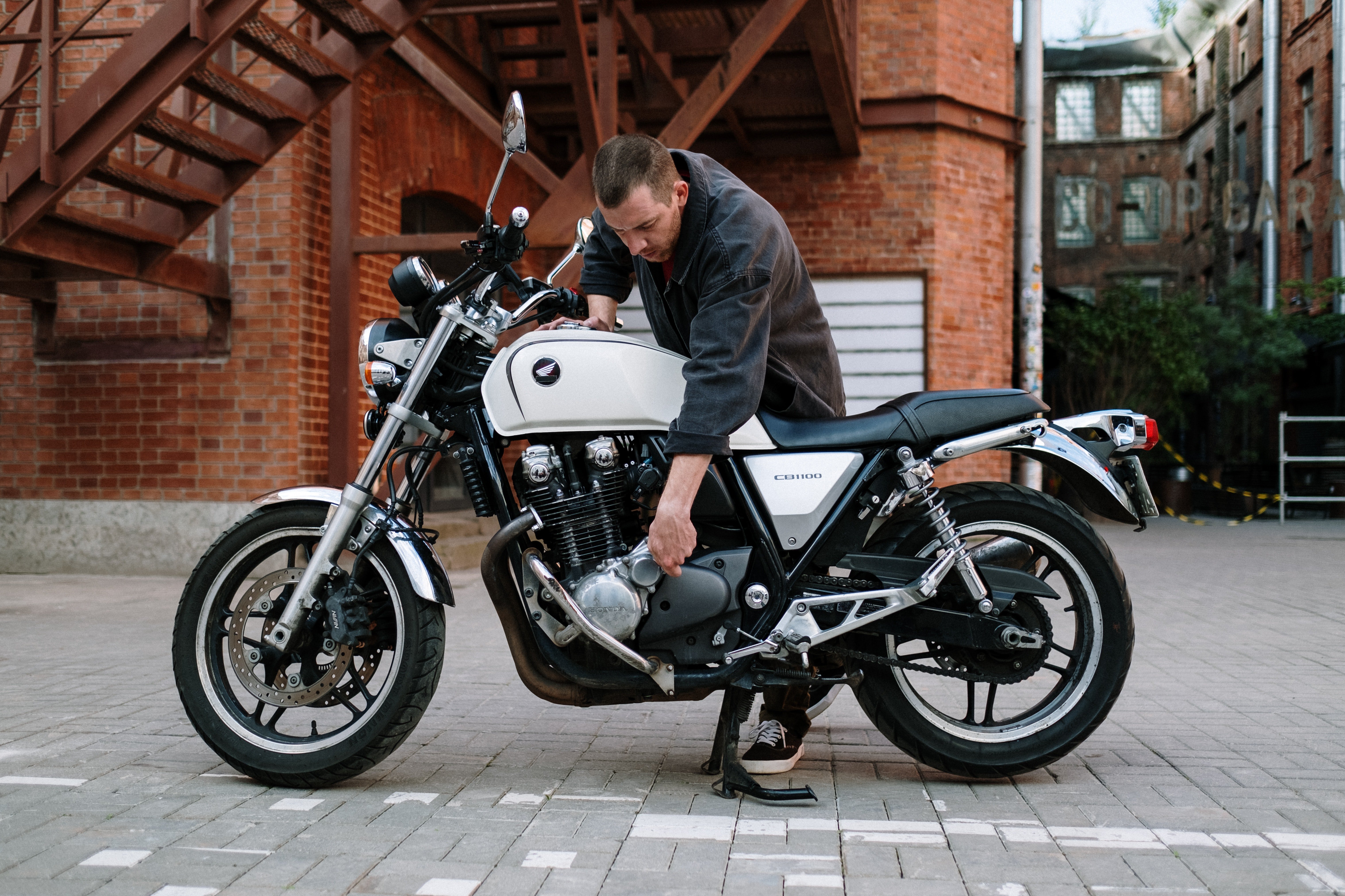 A man standing over his motorbike in front of a building. | Pexels/  cottonbro 