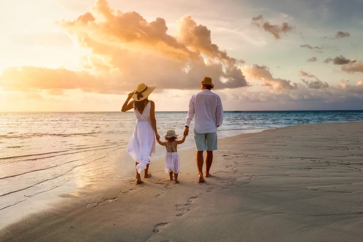 An elegant family in white summer clothing walking hand in hand down a tropical paradise beach during sunset | Source: Shutterstock